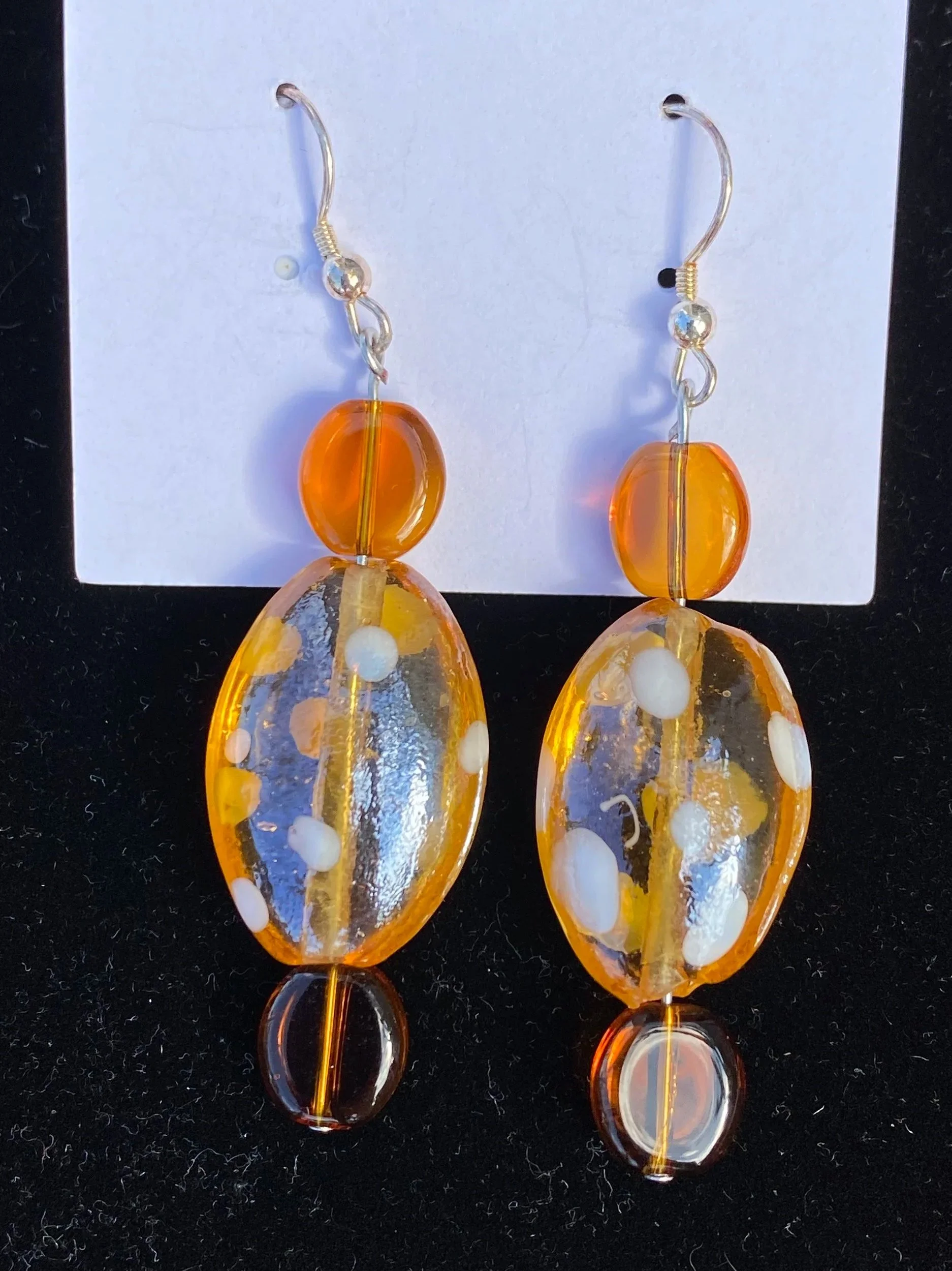 A pair of orange and clear glass dangle earrings with white and gold accents, hanging against a dark background.