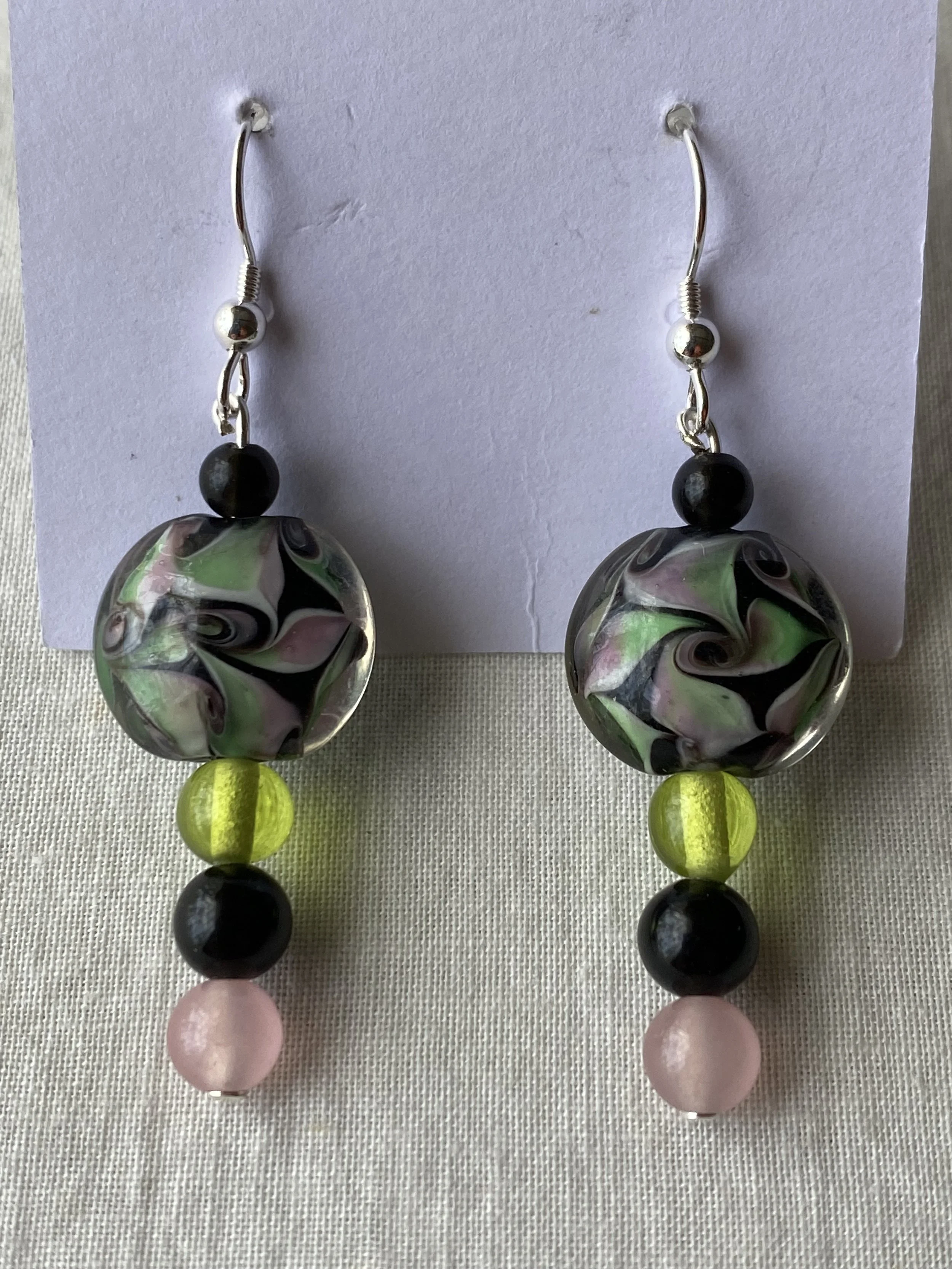 Pair of dangling earrings with black, pink, green, and multicolored glass beads on a white background.