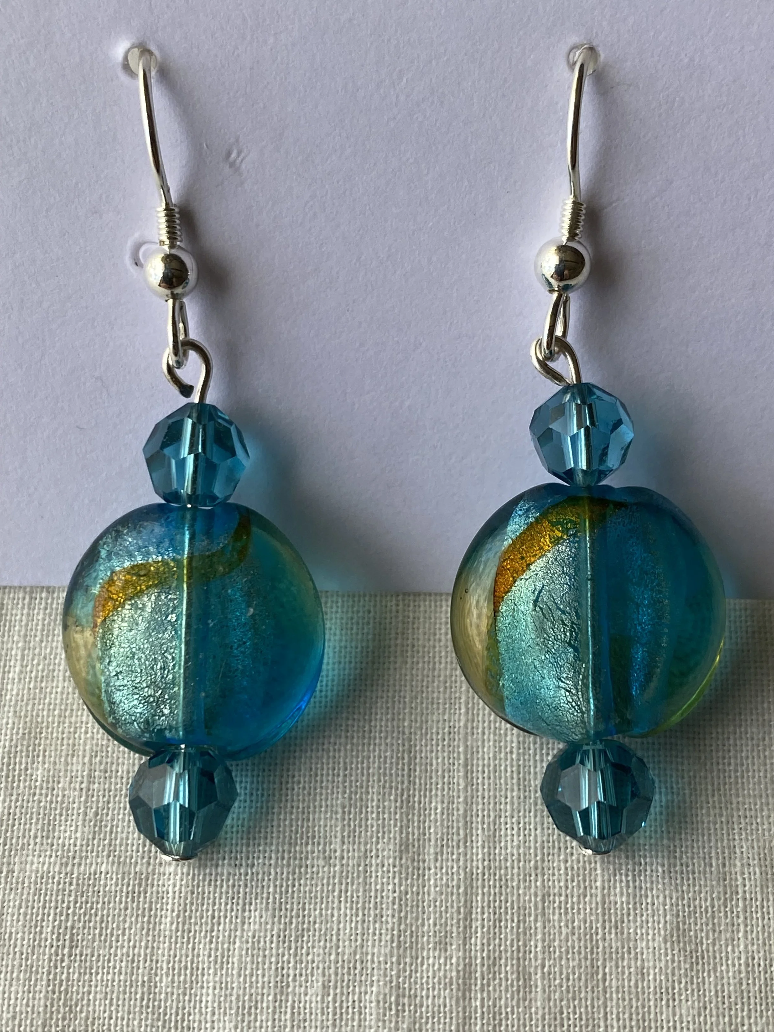 A pair of earrings featuring round blue glass beads with yellow accents, topped with smaller faceted blue beads, hanging from silver hooks.