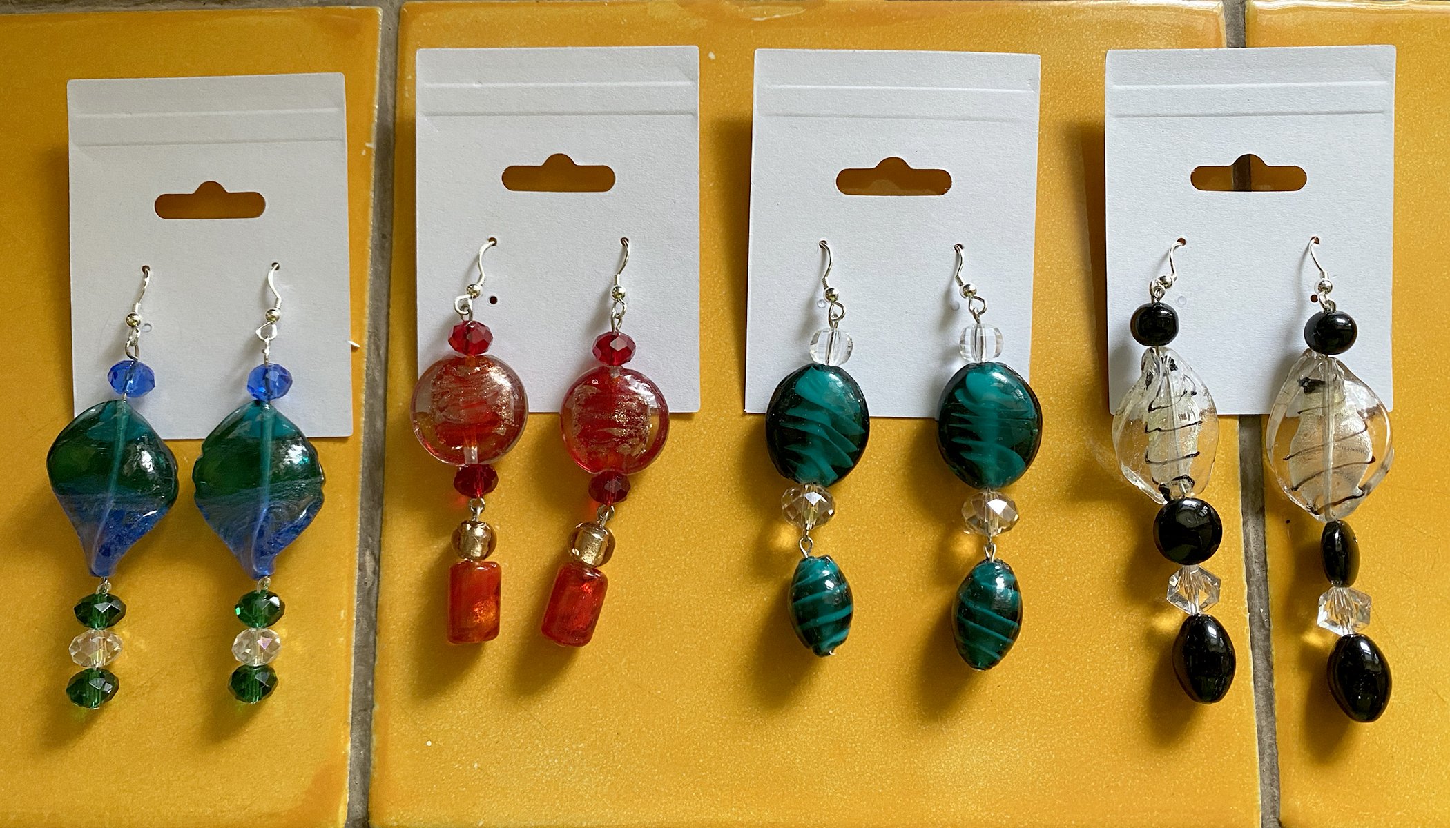 Three white display boards with colorful glass bead earrings on a yellow background.