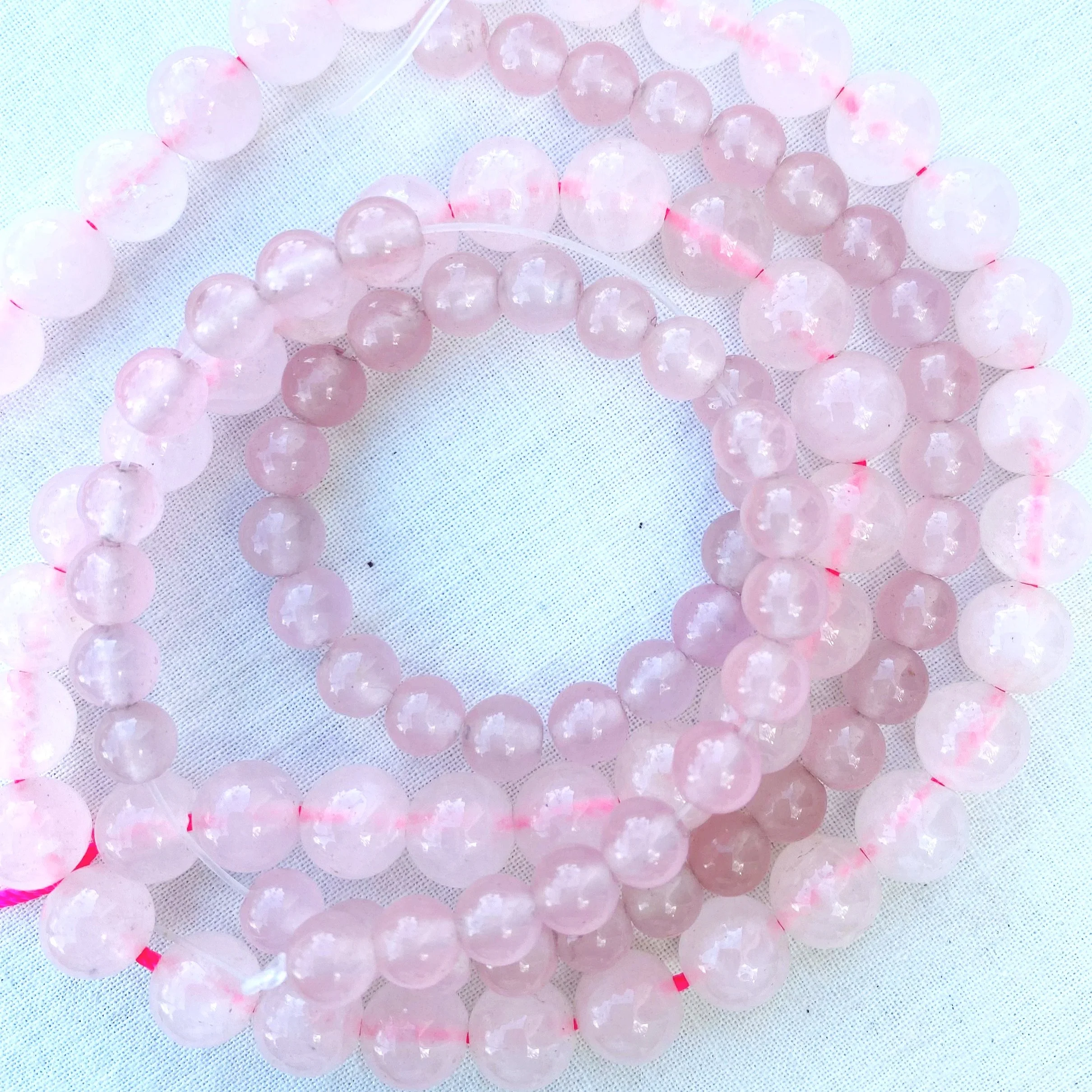 Close-up of multiple pink translucent rose quartz beads on a white mesh surface.
