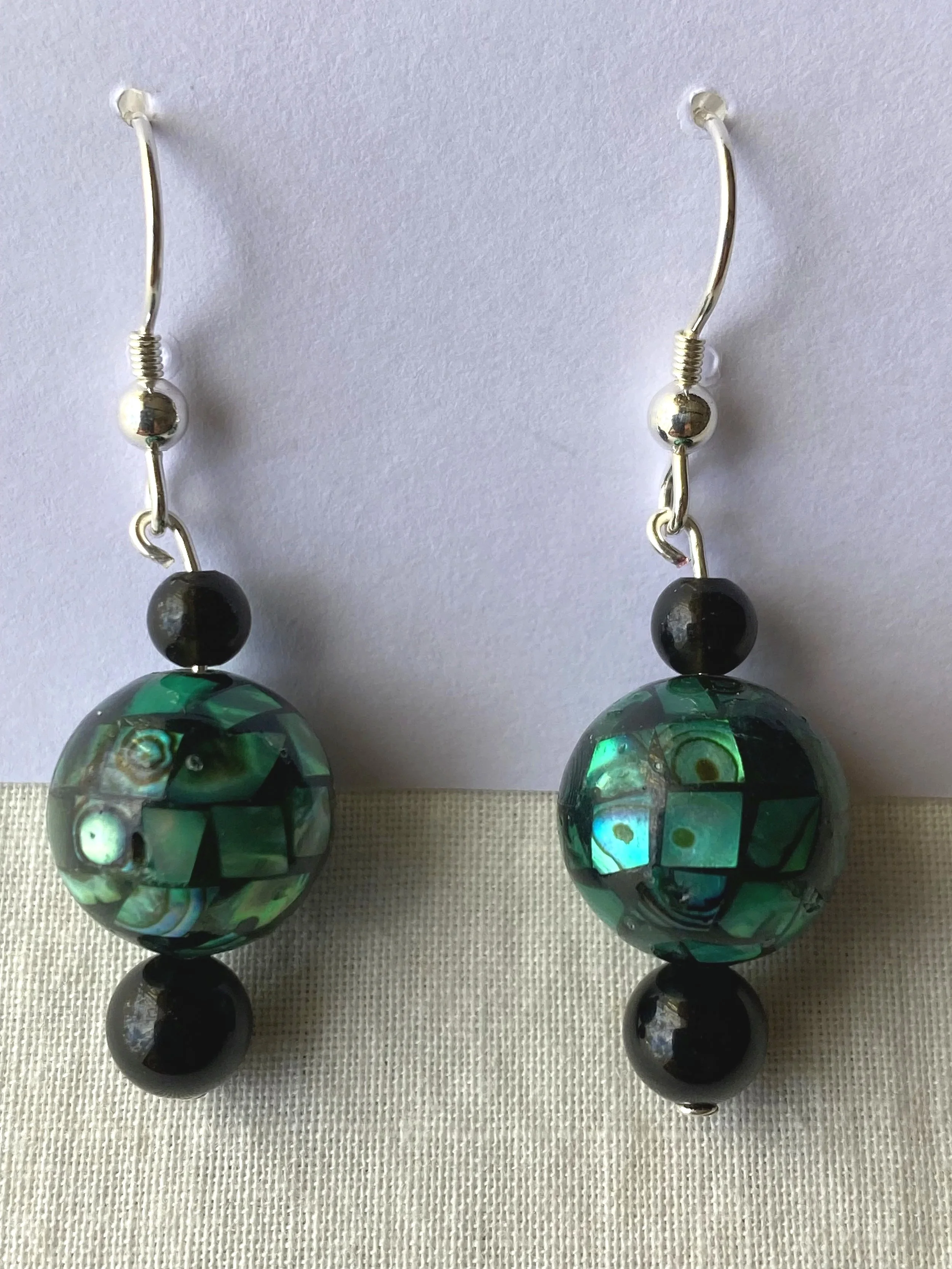 A pair of long dangling earrings with black and green marbled glass beads, metallic silver accents, and hooks, displayed against a light background.