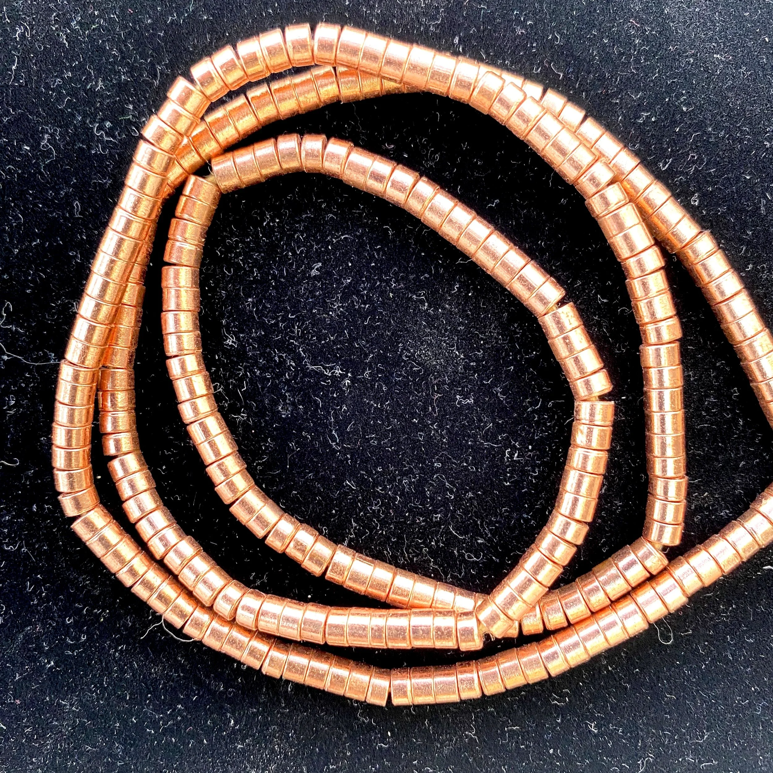 Close-up of multiple copper-colored beads, coiled wires on a black textured surface.