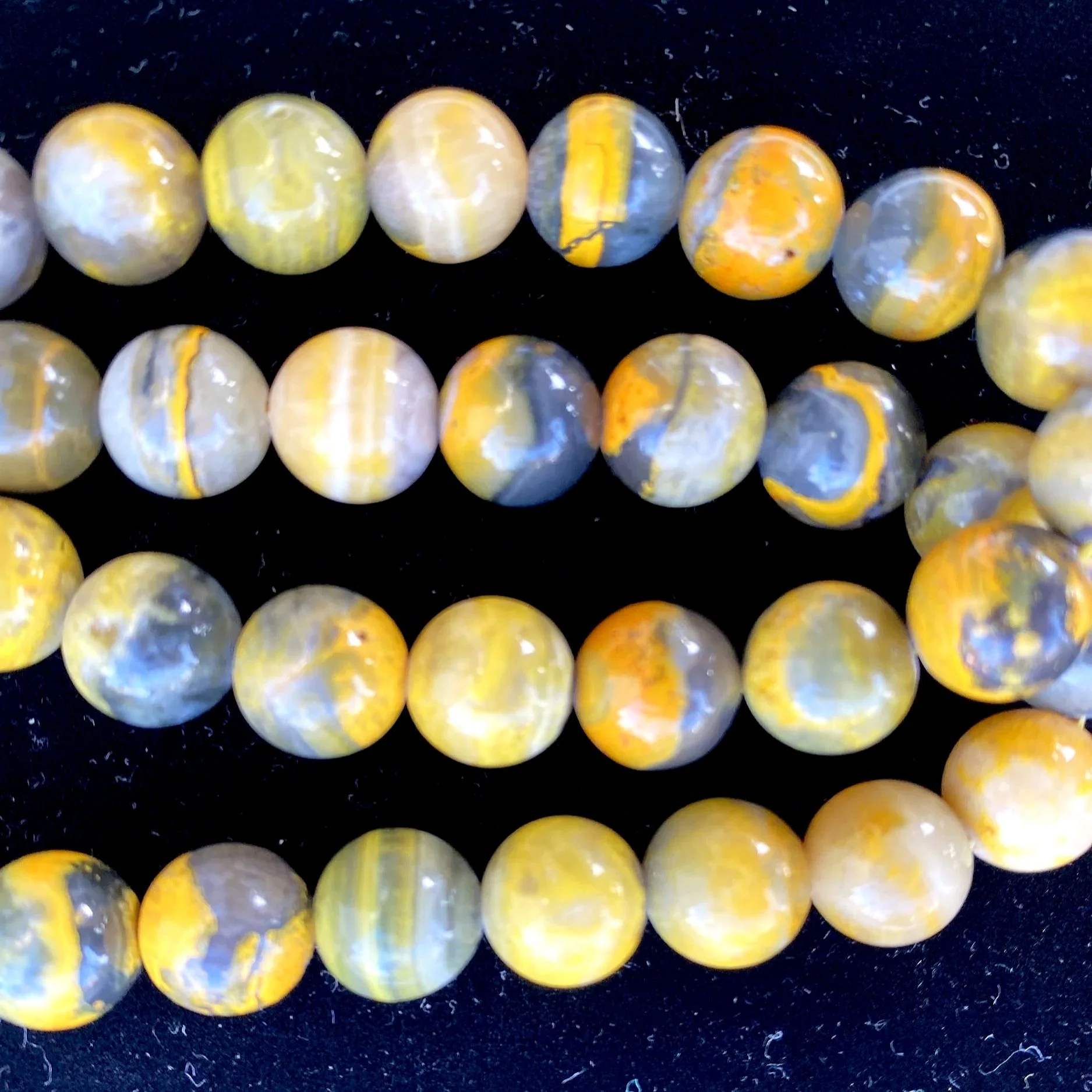 Close-up of a string of round, polished beads with yellow, white, and gray marbled patterns, laid on a black surface.