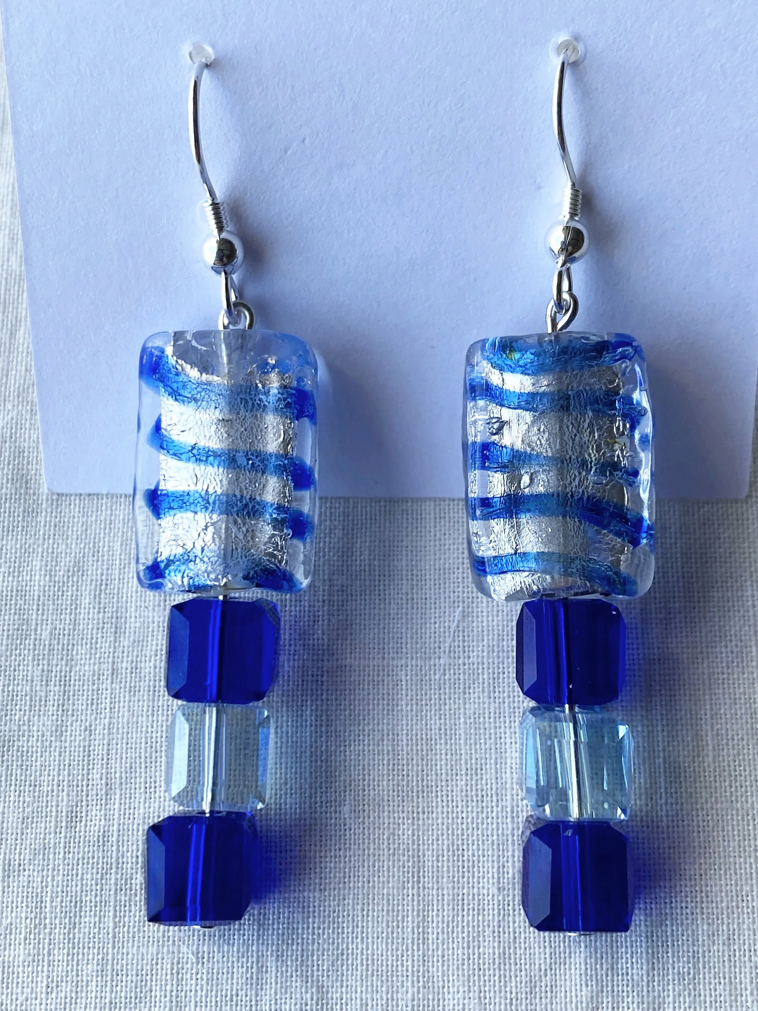 Close-up photo of blue and clear glass earrings with silver hooks on white background.