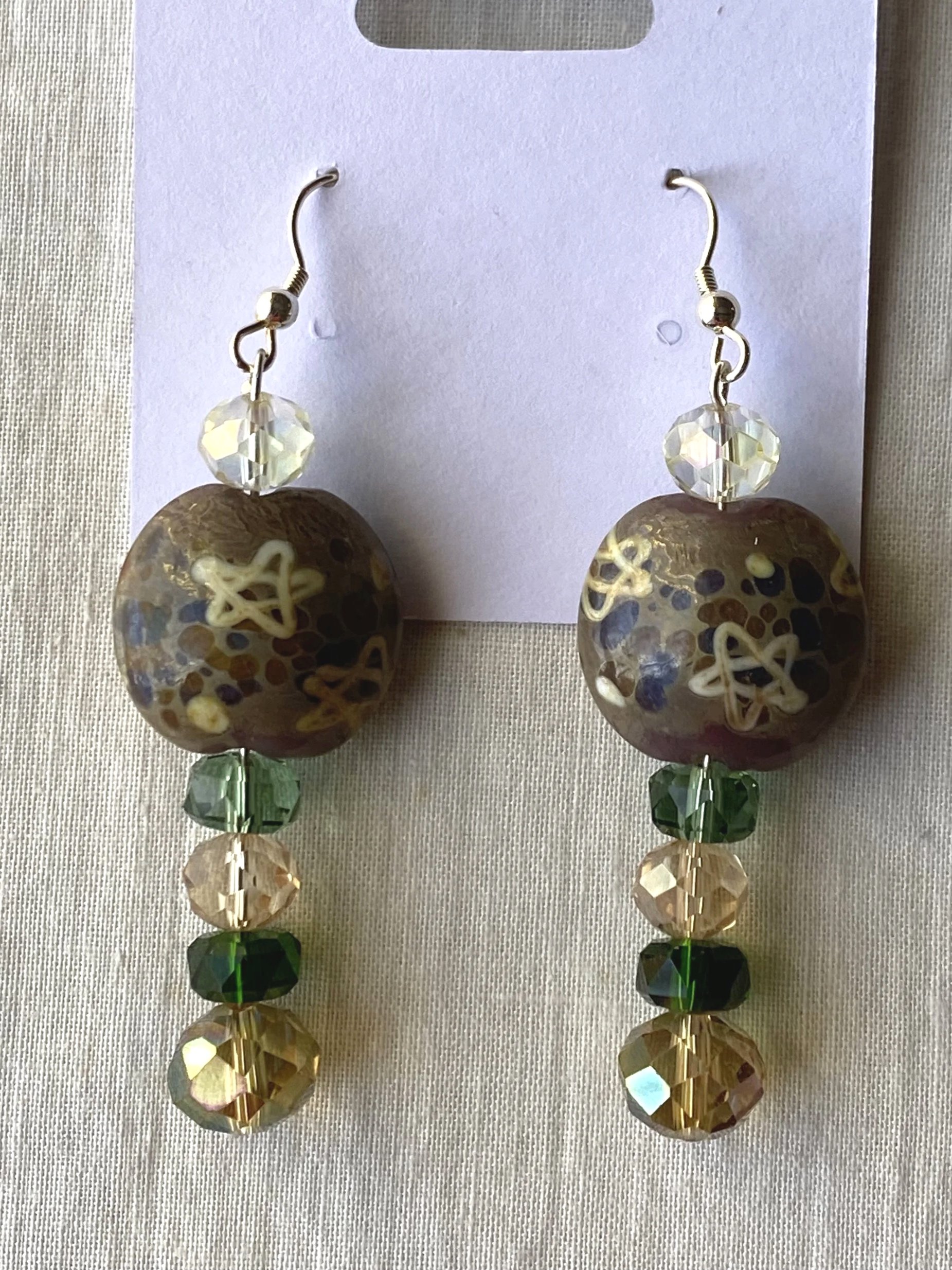 Colorful beaded dangle earrings with large faceted beads in various colors and shapes, including clear, gold, green, and black, attached to metal hooks.