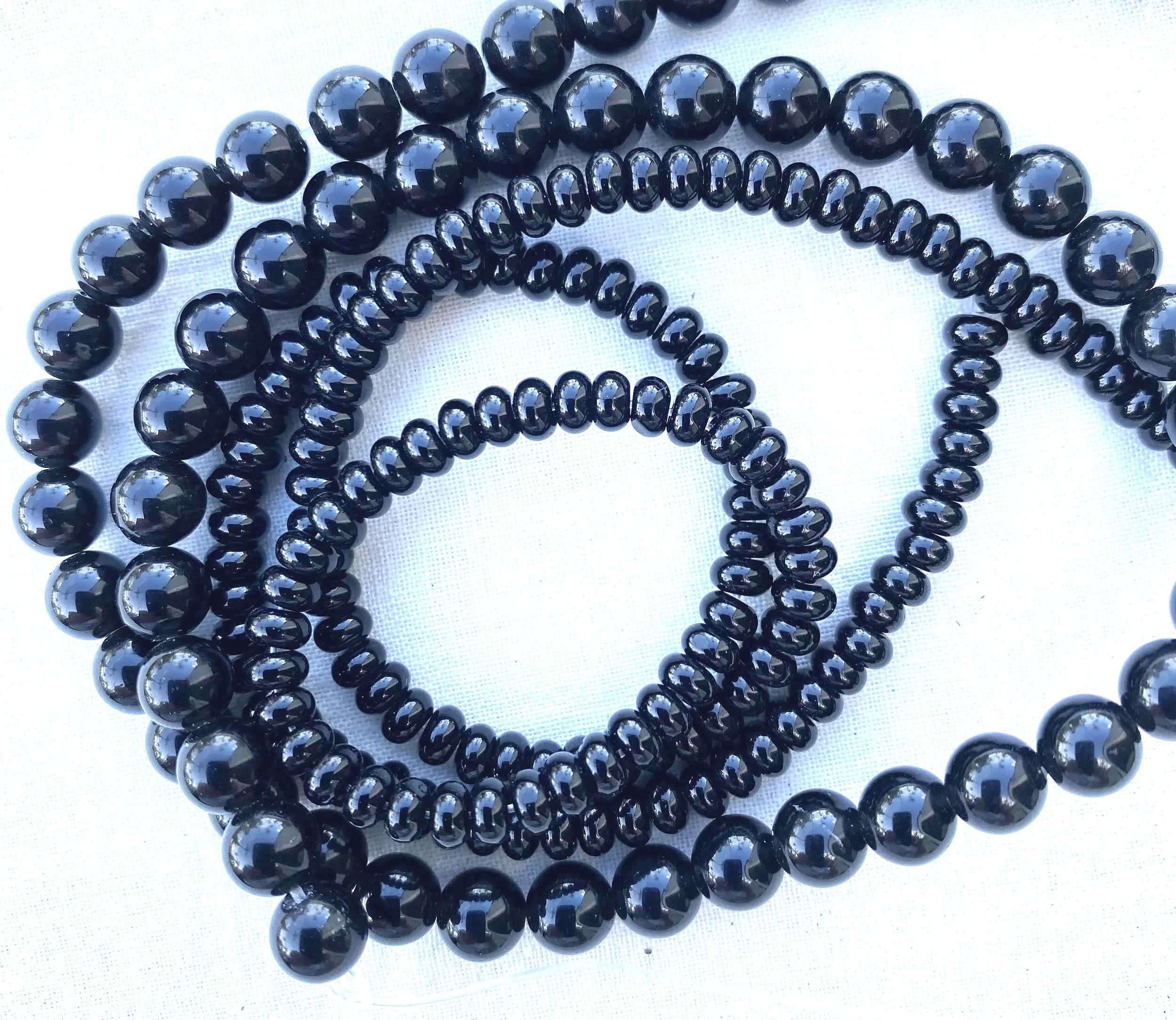 Close-up of several strands of glossy black beads, coiled and layered on a white surface.