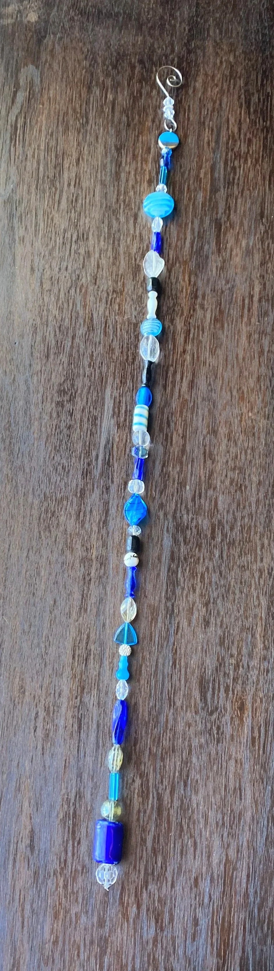 A long beaded necklace with various blue, white, black, and clear beads laid out on a wooden surface.
