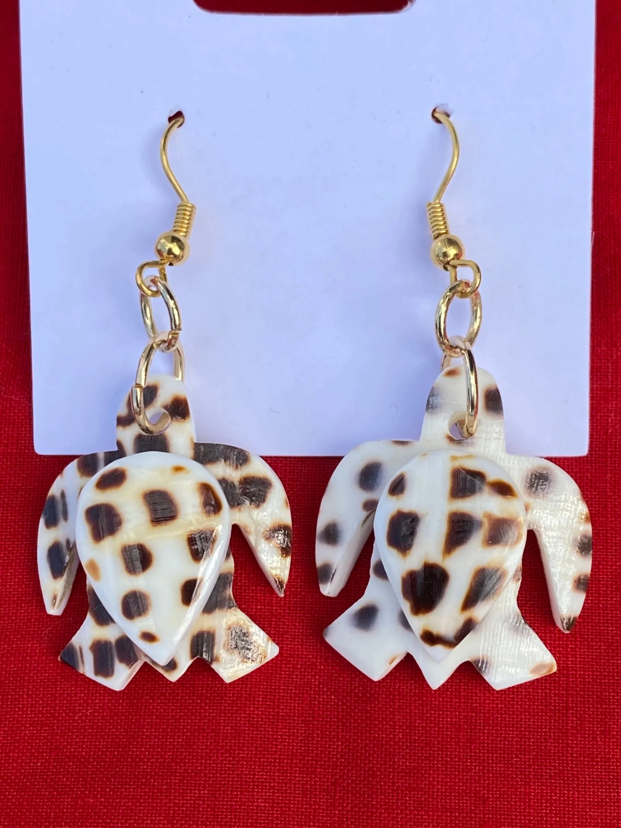 A display of leopard print shell earrings hanging on a white card with a red background.