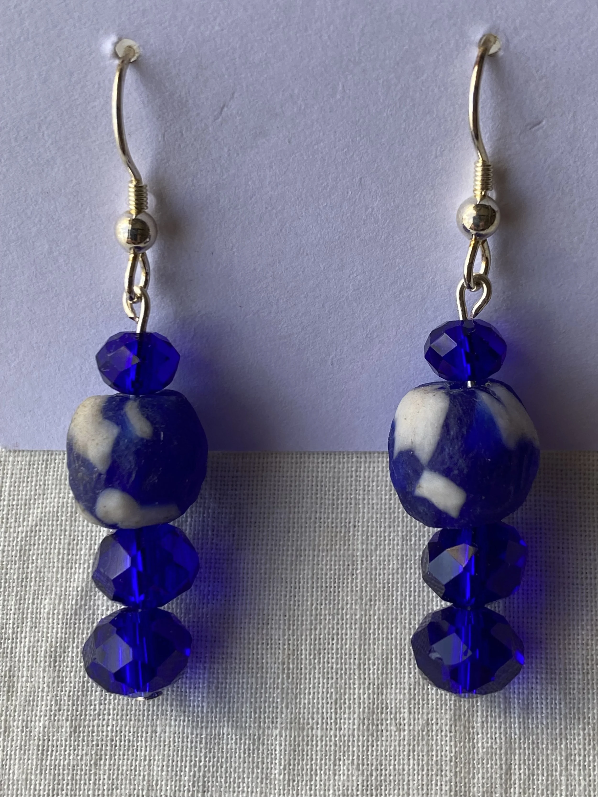 Silver earrings with blue beads hanging from silver hooks on a white background.