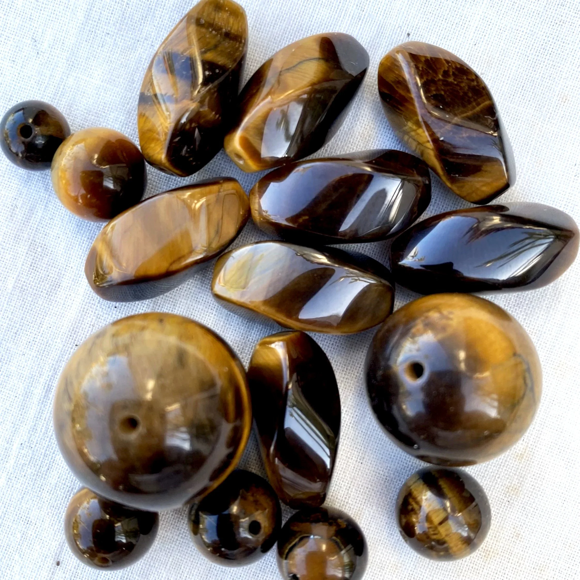 A collection of polished tiger's eye beads arranged on a white fabric background.