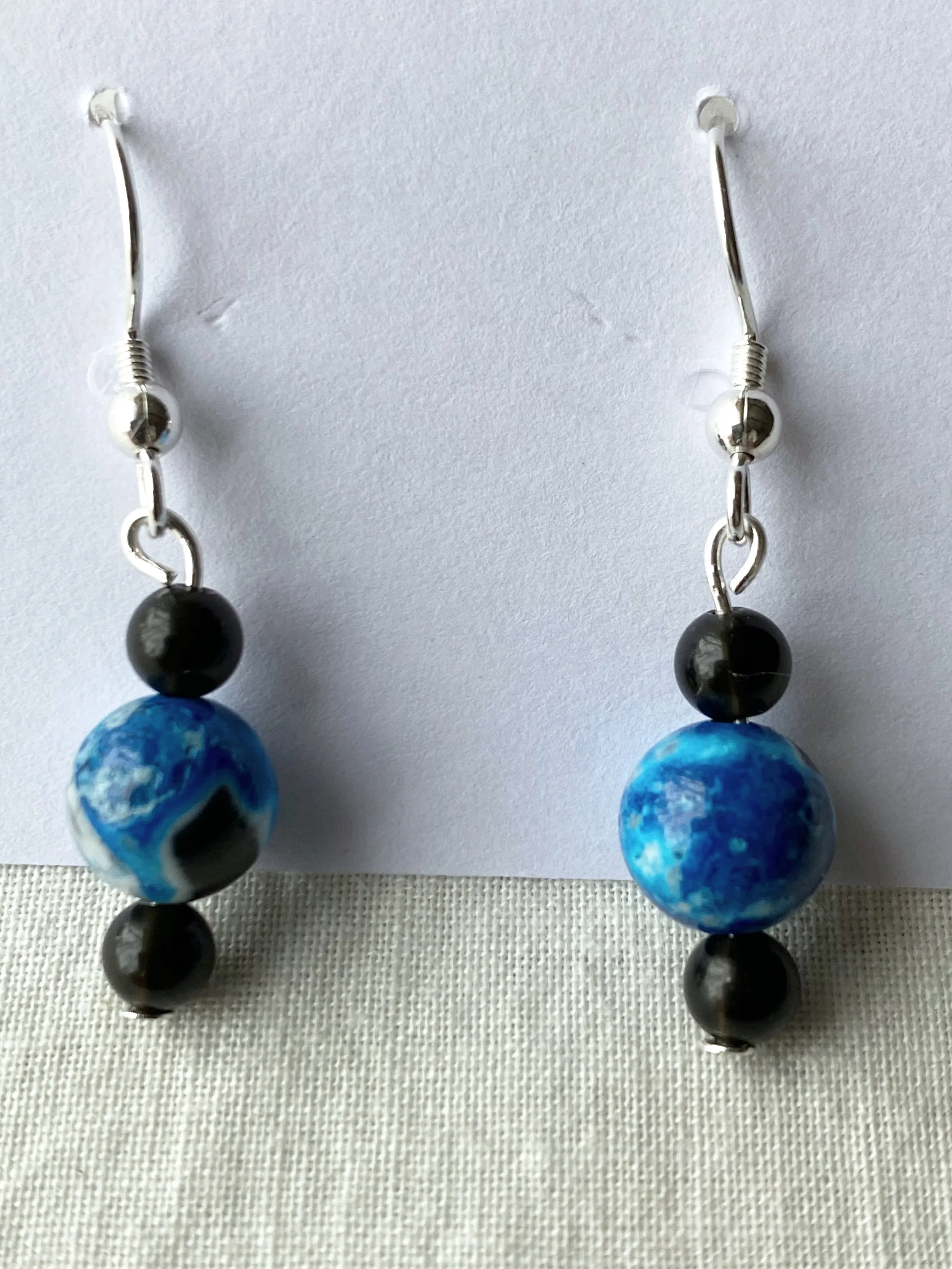 Pair of drop earrings with black and blue marbled beads, silver hooks, and decorative silver rounds.