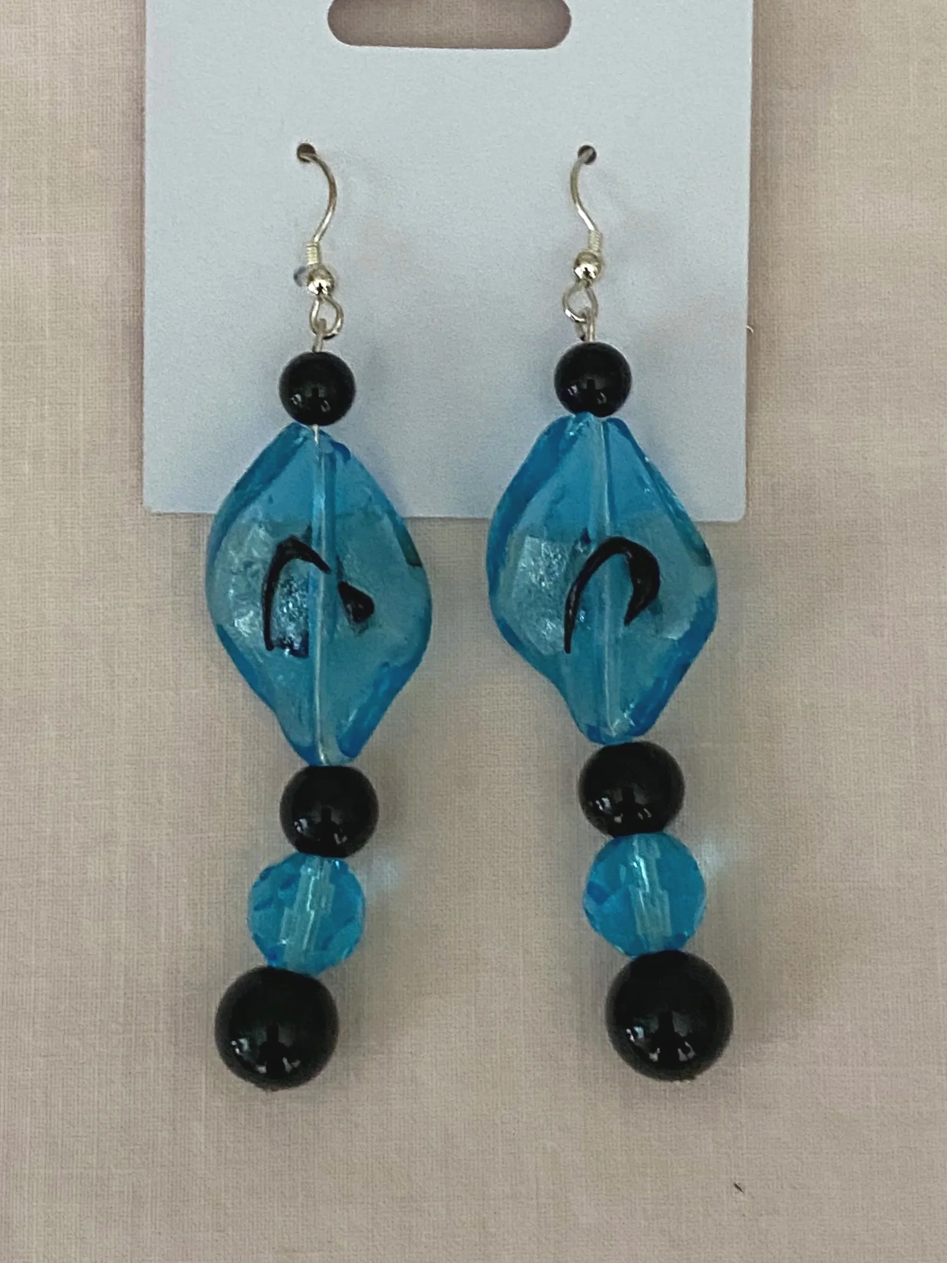 Beaded earrings with blue, black, and clear beads hanging on a white display card.