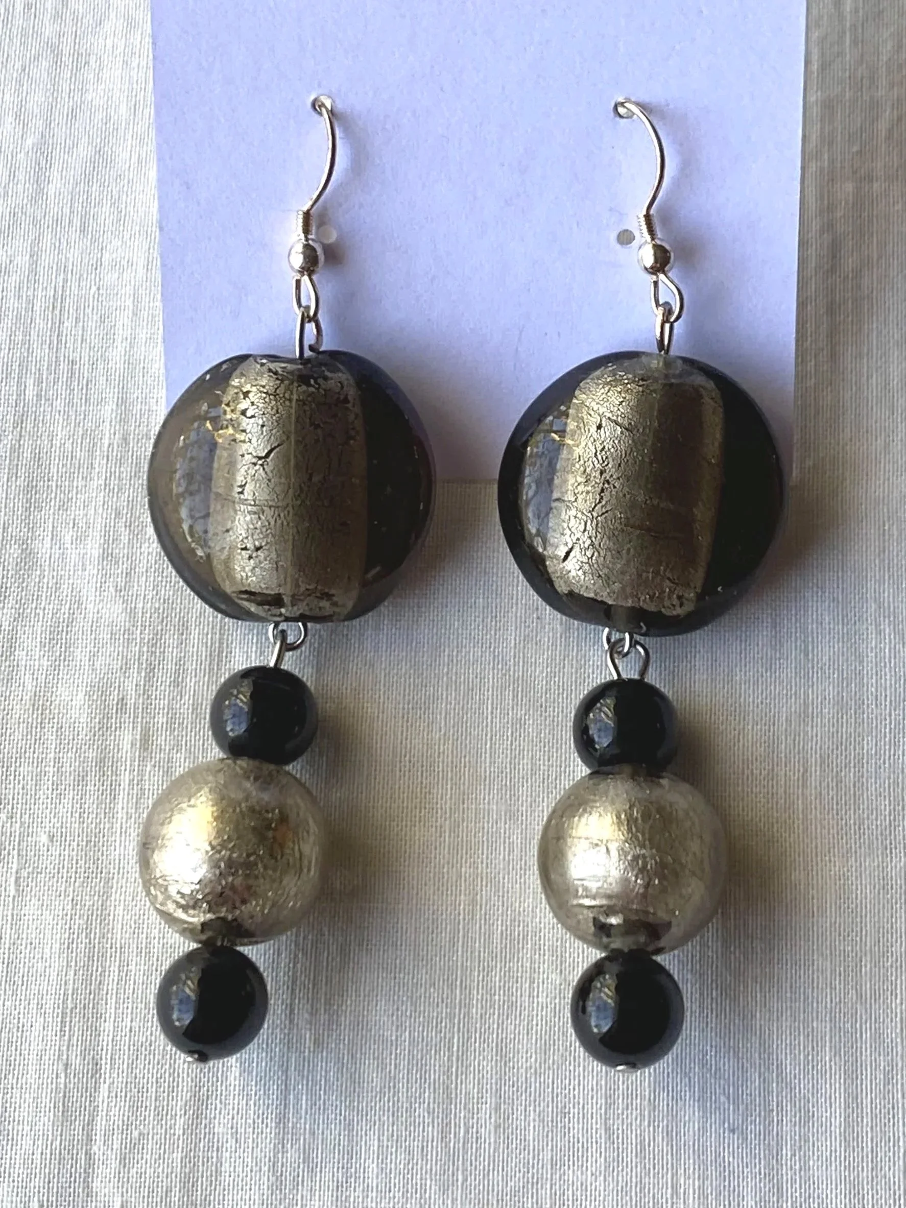 Silver and black dangling earrings with gold and black spherical beads, hanging against a white background.