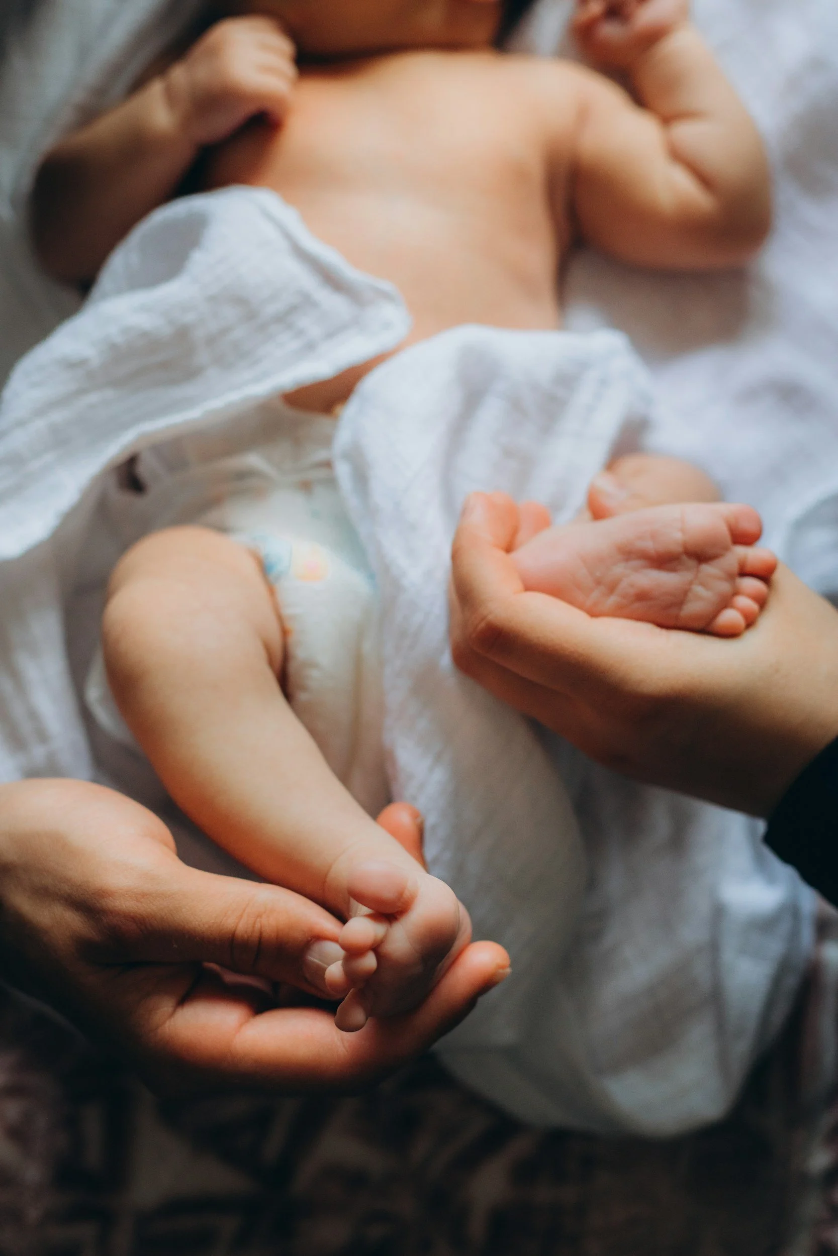 A close-up of a baby's hand and arm being gently held by an adult's hand.