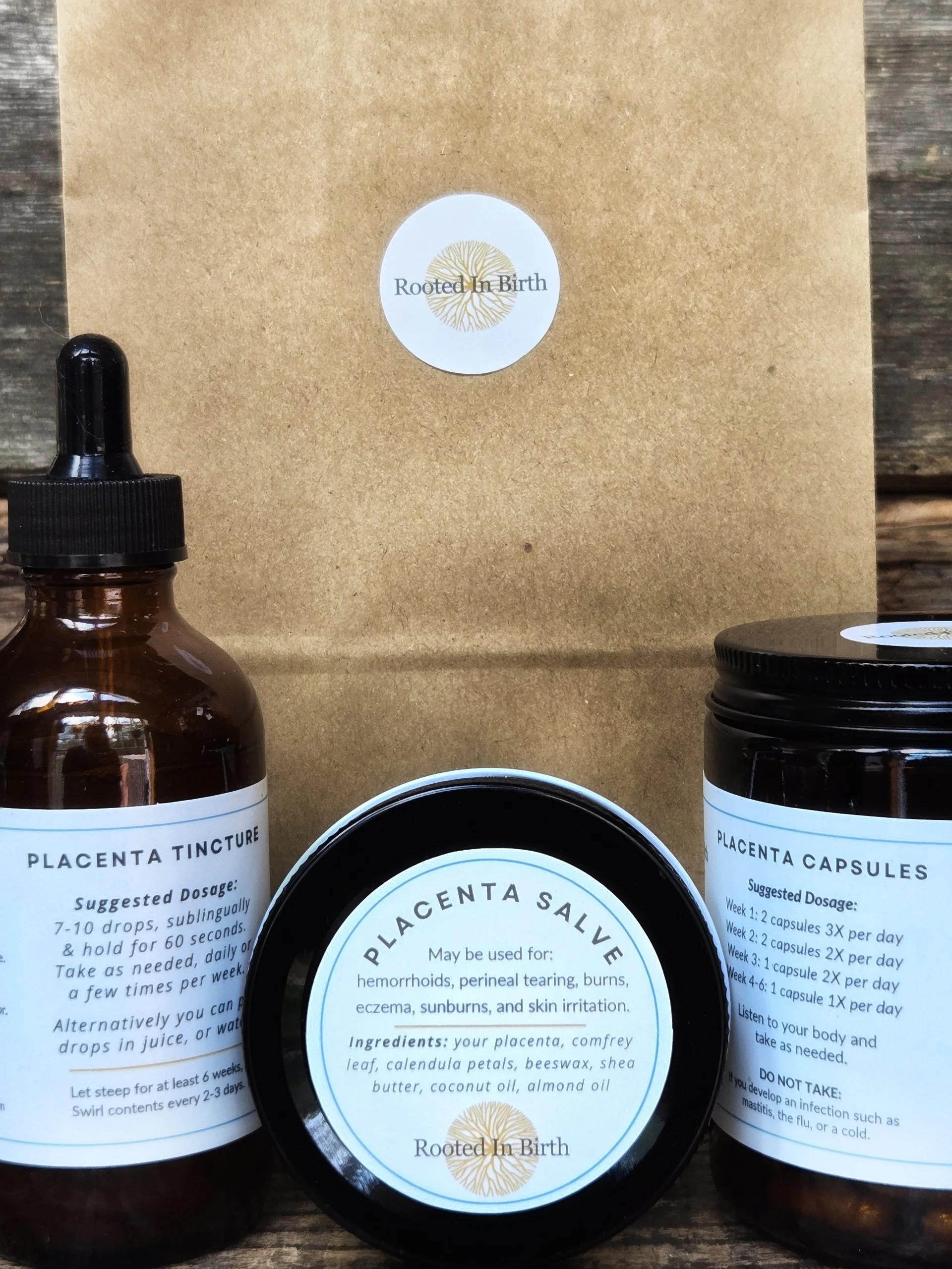 Bottles of placenta tincture and placenta capsules with labels from Rooted In Birth, placed on a wooden surface.
