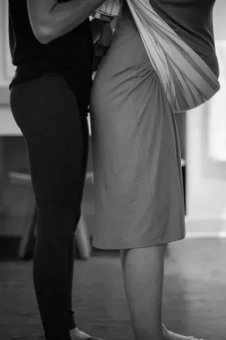 Close-up of two people standing indoors, one holding a bag and the other wearing a long skirt.