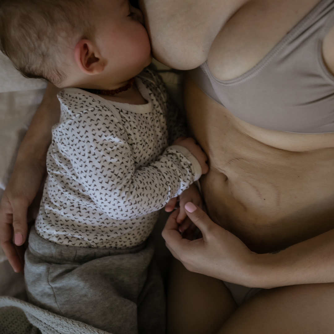 A child breastfeeding from a woman, with the child's head resting against the woman's chest and her hand gently holding the woman's hand.