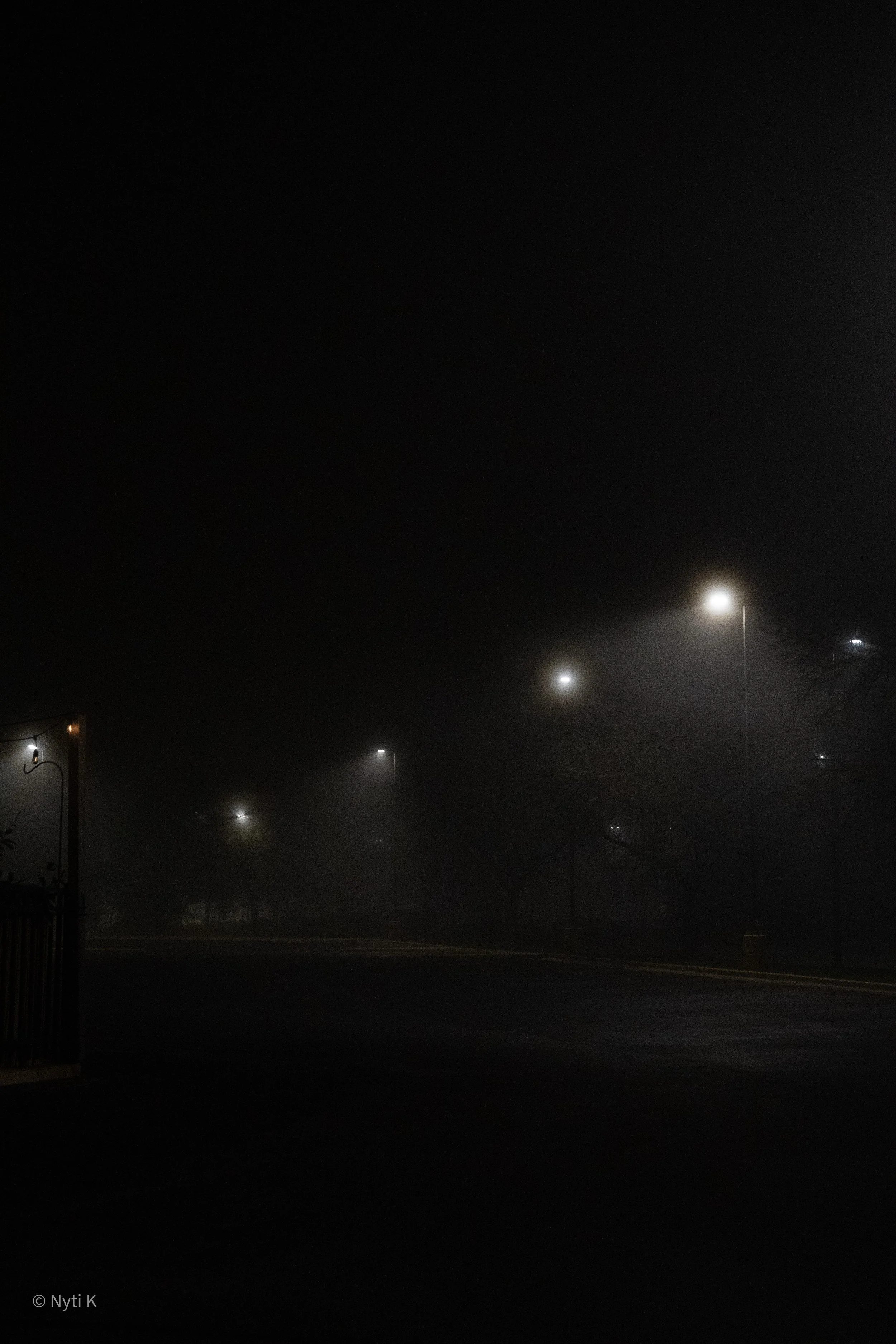 A foggy night scene with streetlights illuminating a foggy street, creating a hazy glow in the darkness.