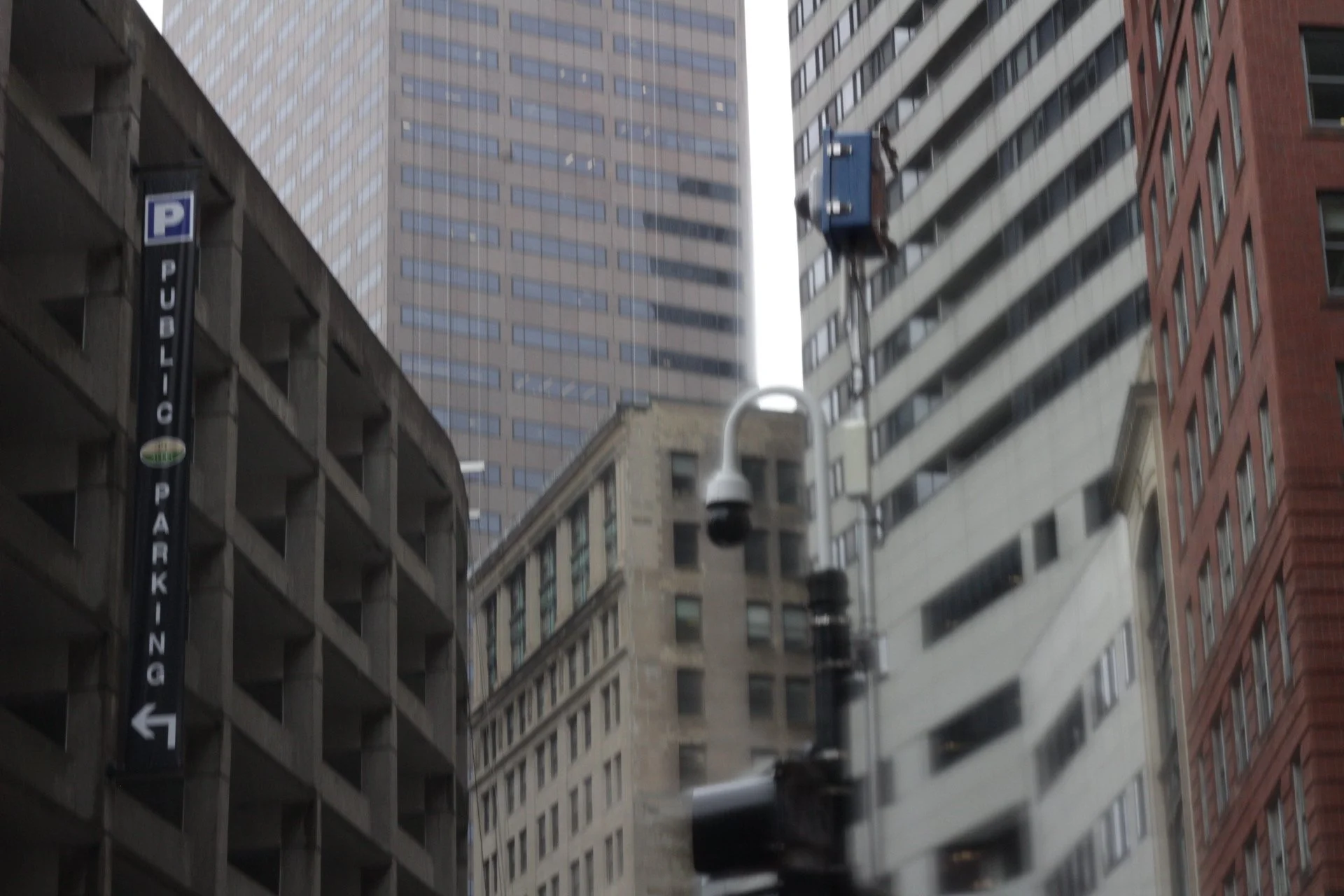 City street view looking up at tall buildings with a parking sign on the left and a street lamp in the center.