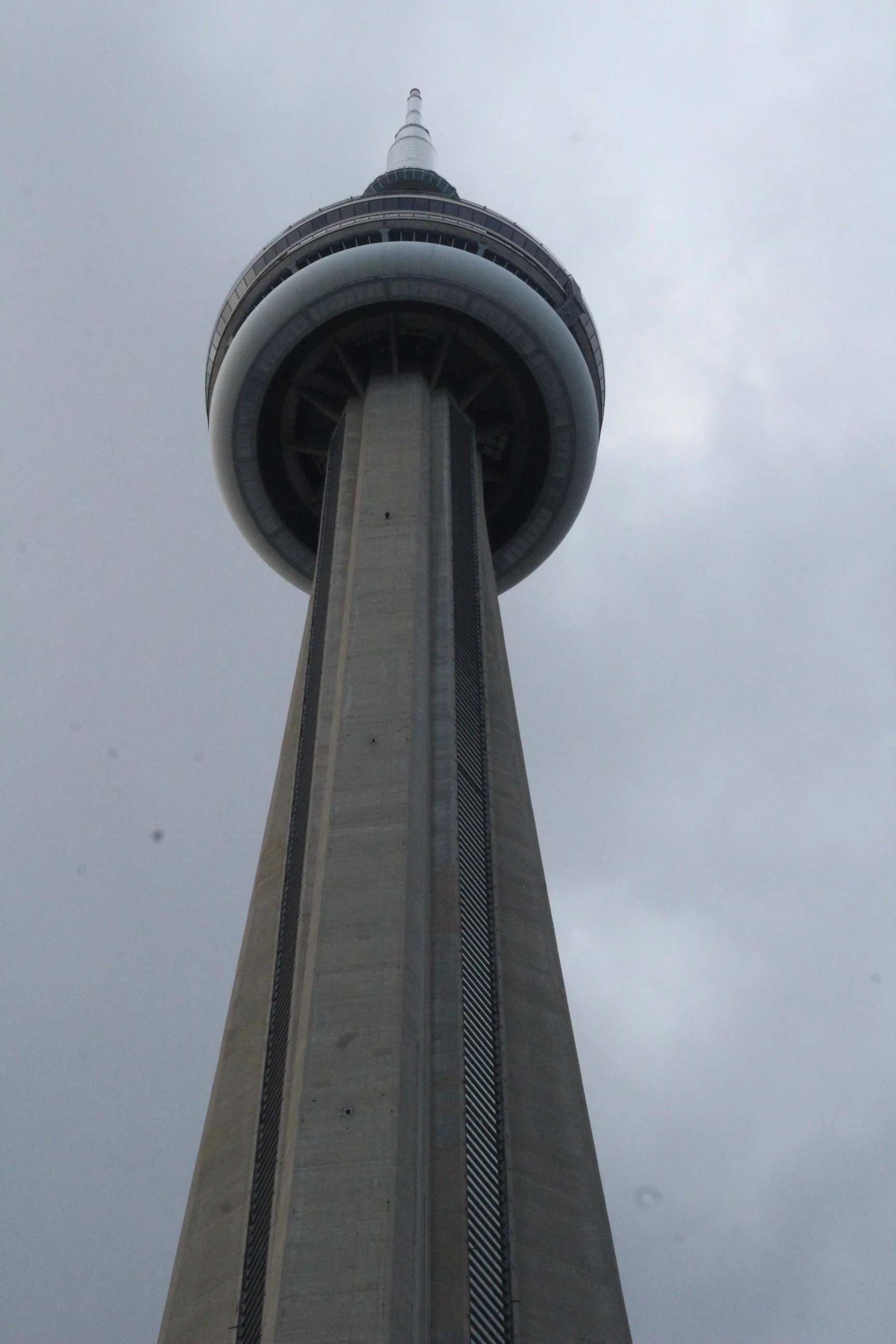 A tall tower viewed from below, with a rounded observation deck near the top and a spire extending upward, set against a cloudy sky.