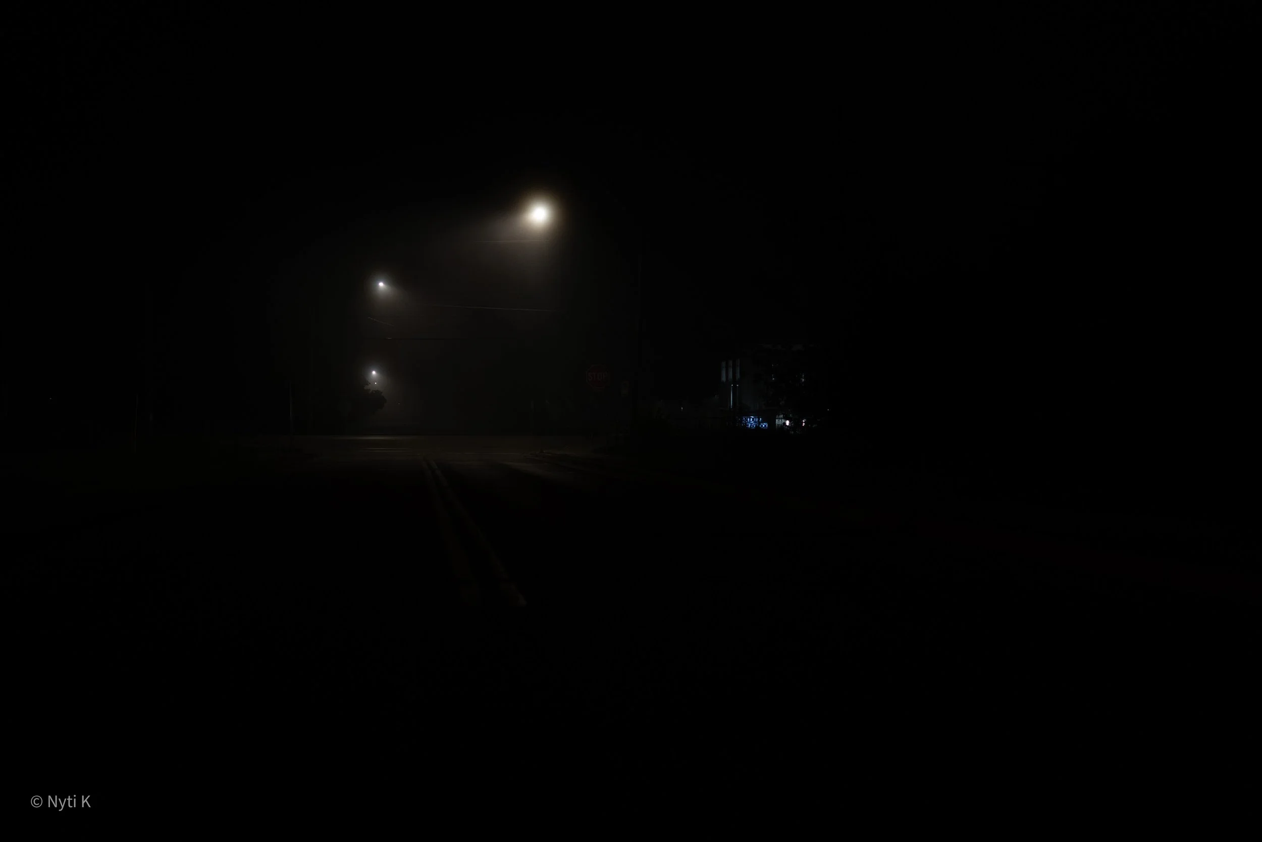 Nighttime scene with streetlights illuminating a dark road, visible moon in the sky, and some faint building lights in the distance.