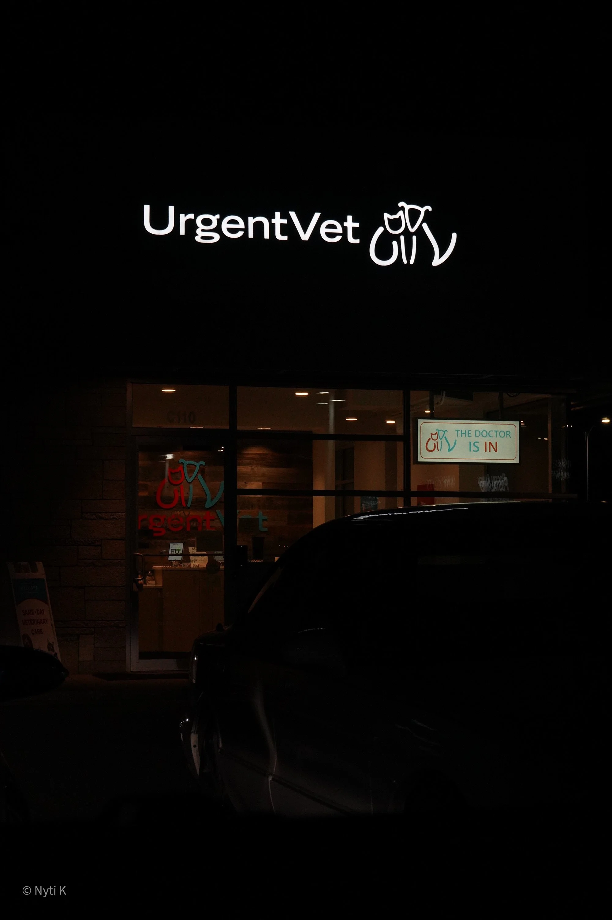 Illuminated sign reading 'Urgent Vet' with an outline of a dog and a cat, outside a veterinary clinic at night.