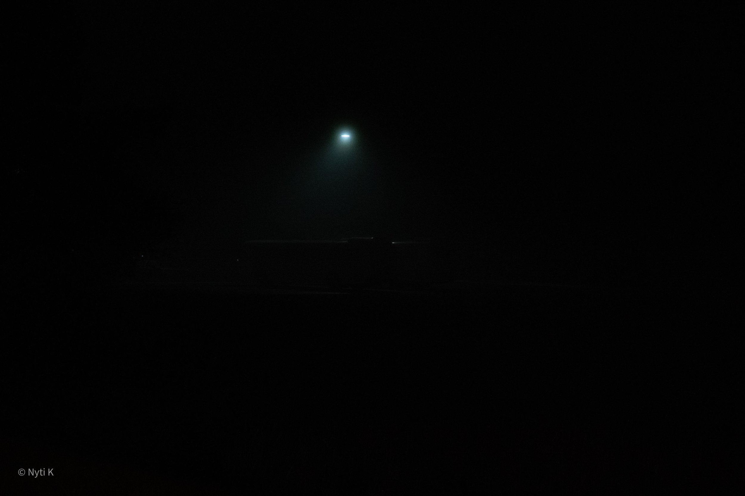 Dark night sky with a bright object resembling a comet or spacecraft emitting a glow and a trail of light.
