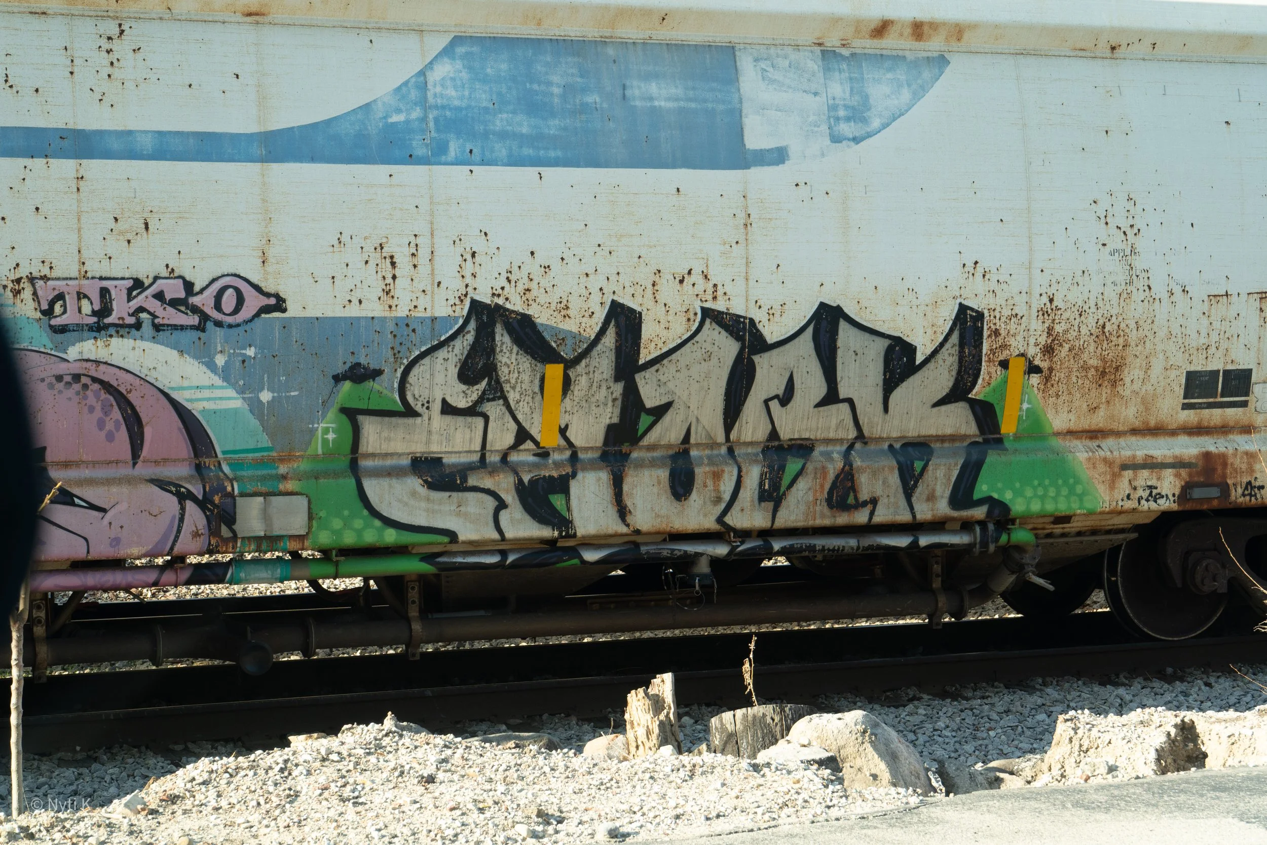 Graffiti on the side of a weathered, rusty train car, featuring various colorful tags and designs.