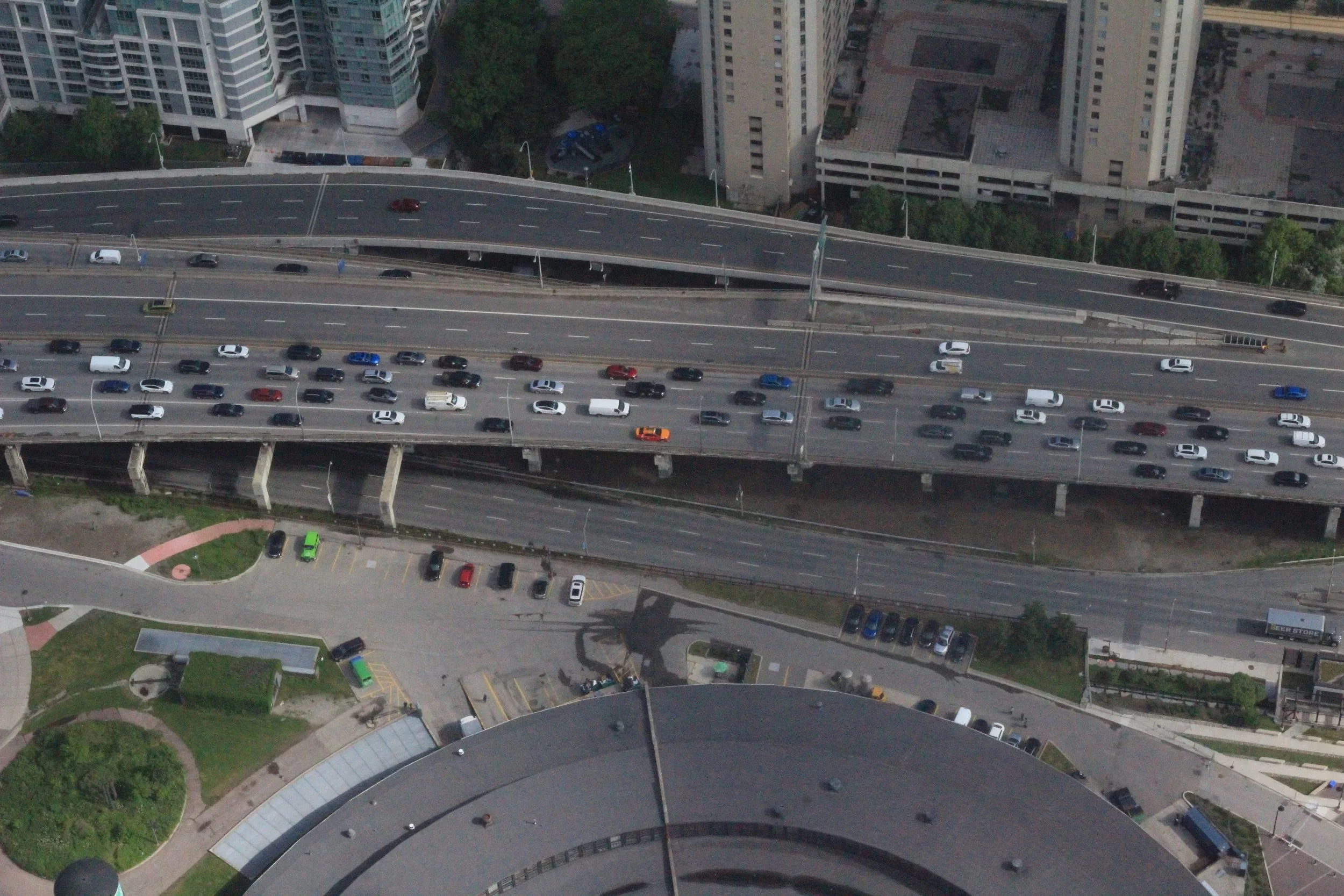 Aerial view of a multi-level highway with numerous cars, surrounded by tall office buildings and greenery.