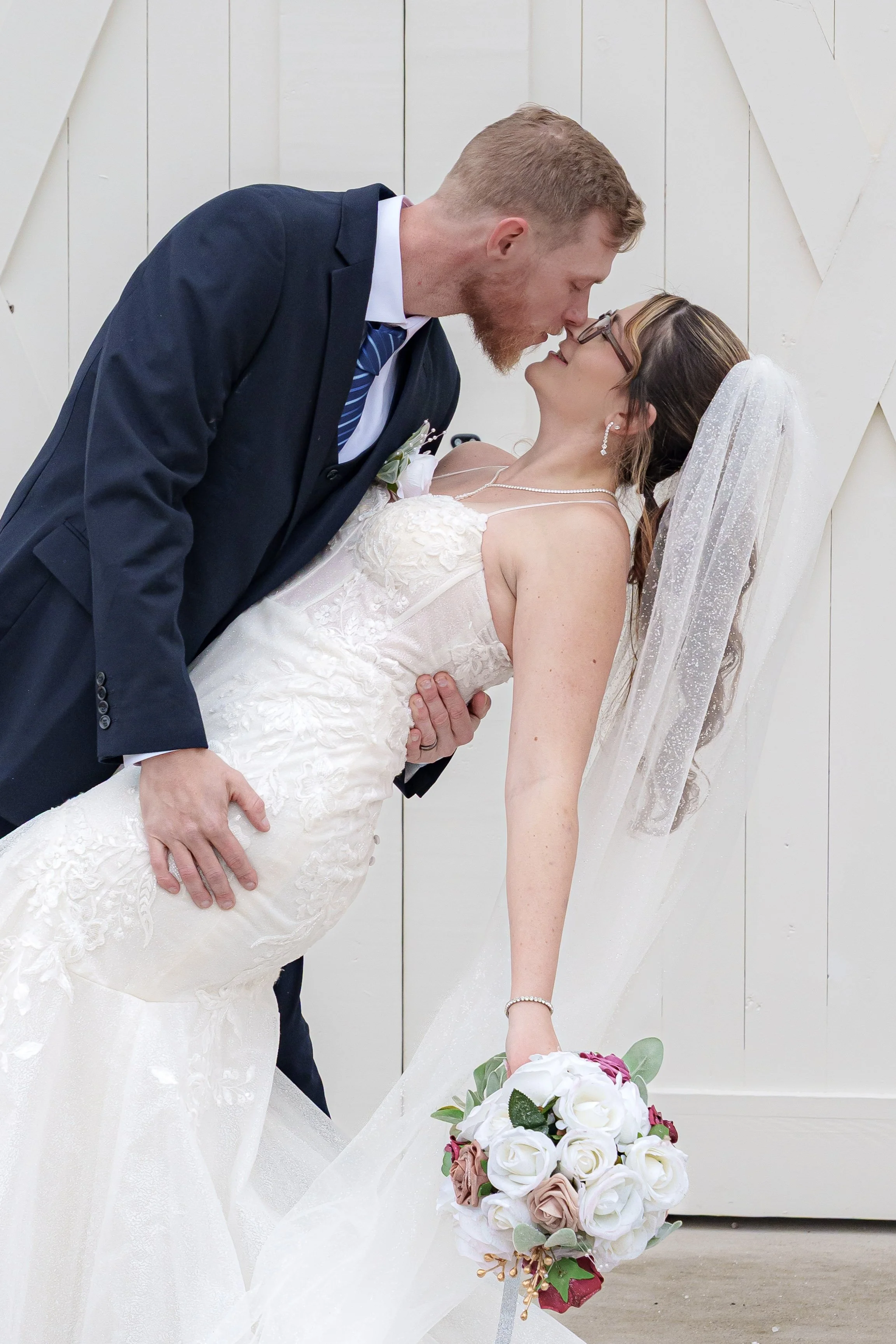 A bride and groom sharing a moment during their wedding, with the groom leaning over the bride who is holding a bouquet of flowers.