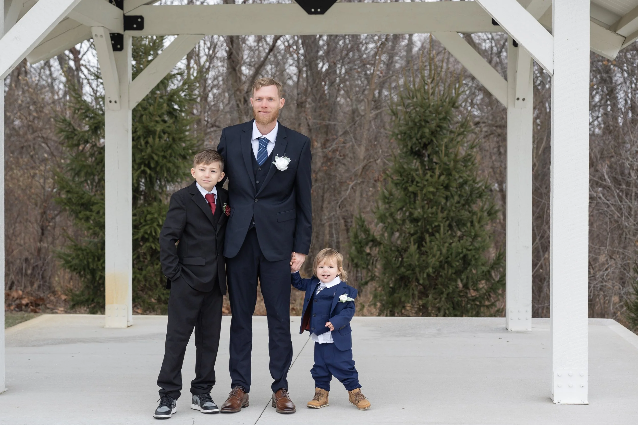 A man and three children dressed in formal clothing, standing under a white gazebo outdoors, with trees in the background.