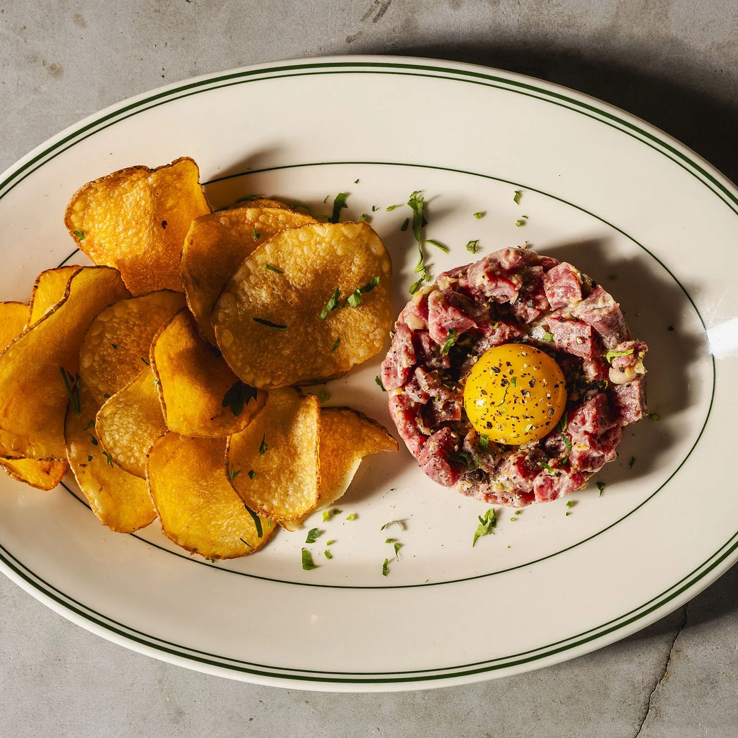 Plate with roasted potato chips and steak tartare topped with a raw egg yolk.