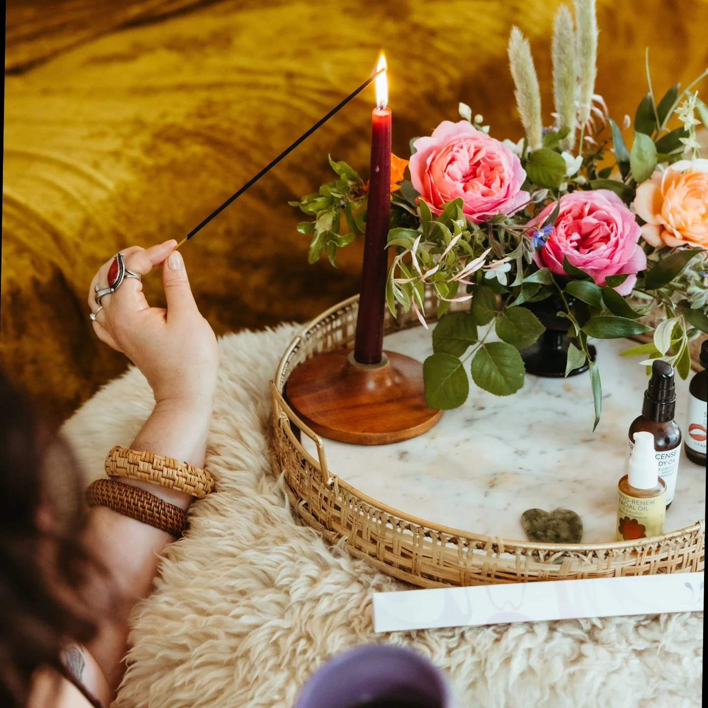 Woman's hand lighting a red candle on a marble tray next to a vase of flowers
