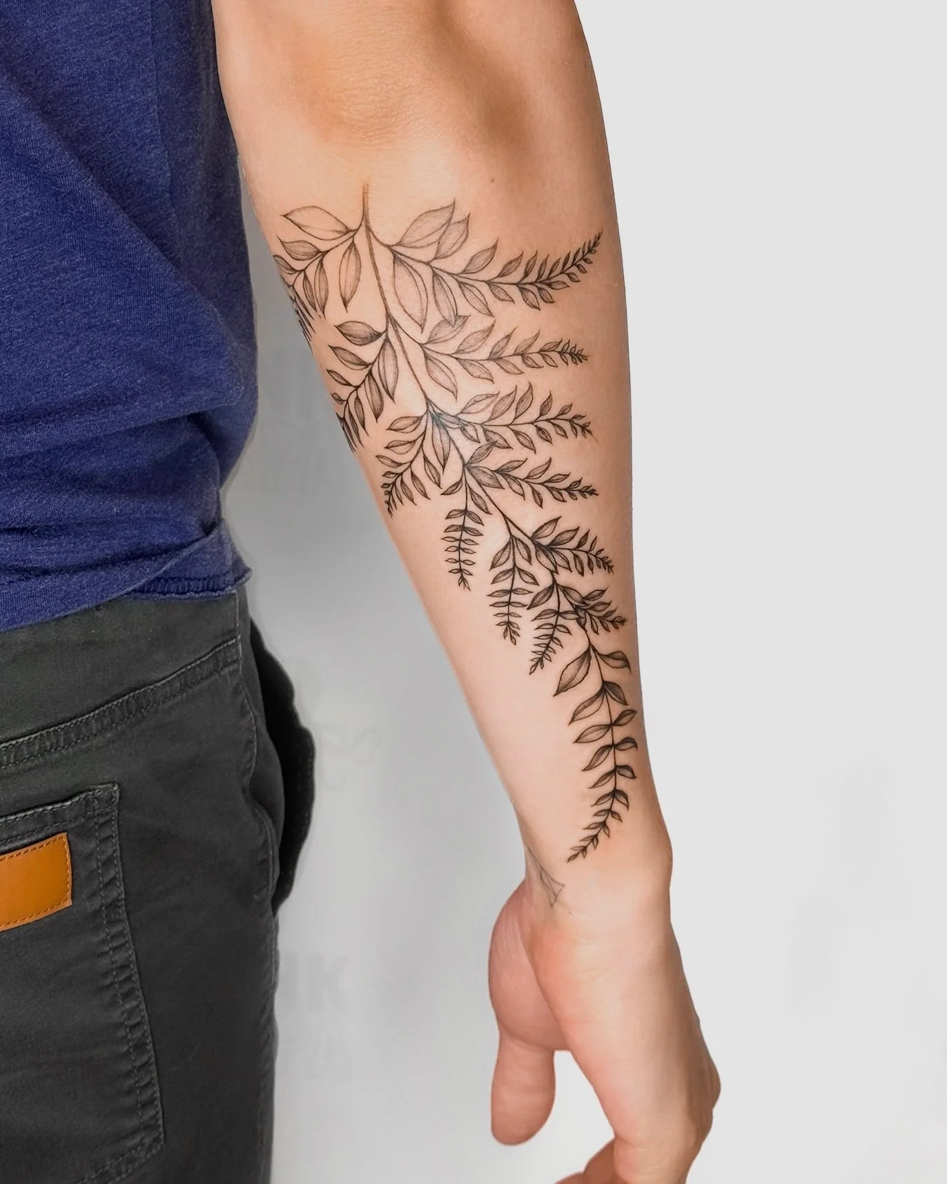 A person's arm with a large, intricate black ink tattoo of branches and leaves extending from the upper arm down to the wrist.