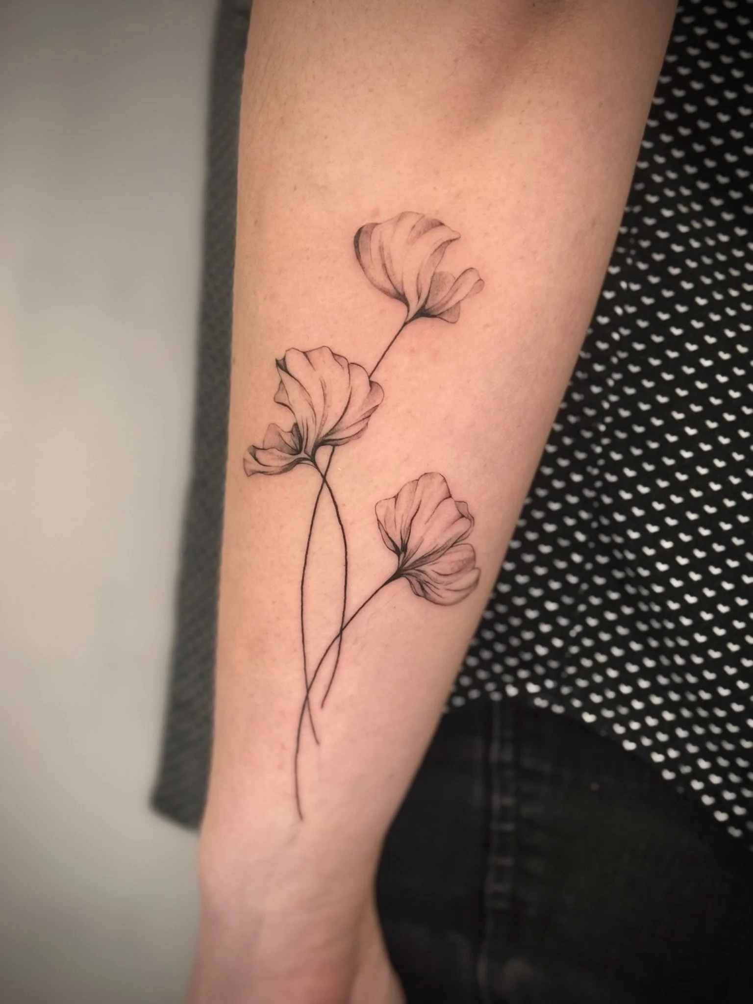 Black ink tattoo of three ginkgo leaves on a person's inner forearm.