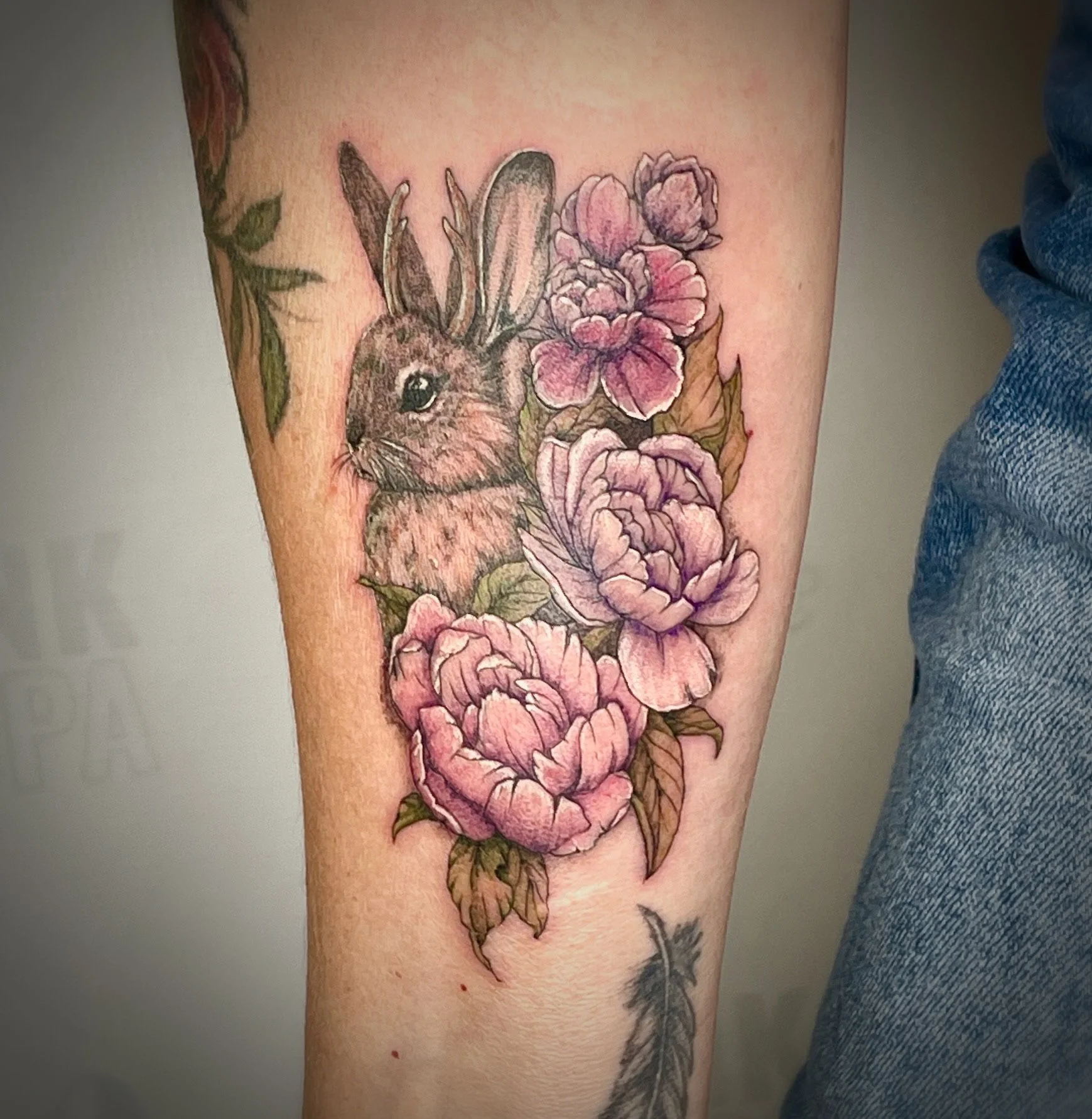 Colorful fine-line tattoo of a rabbit with pink flowers and green leaves on a person's arm.