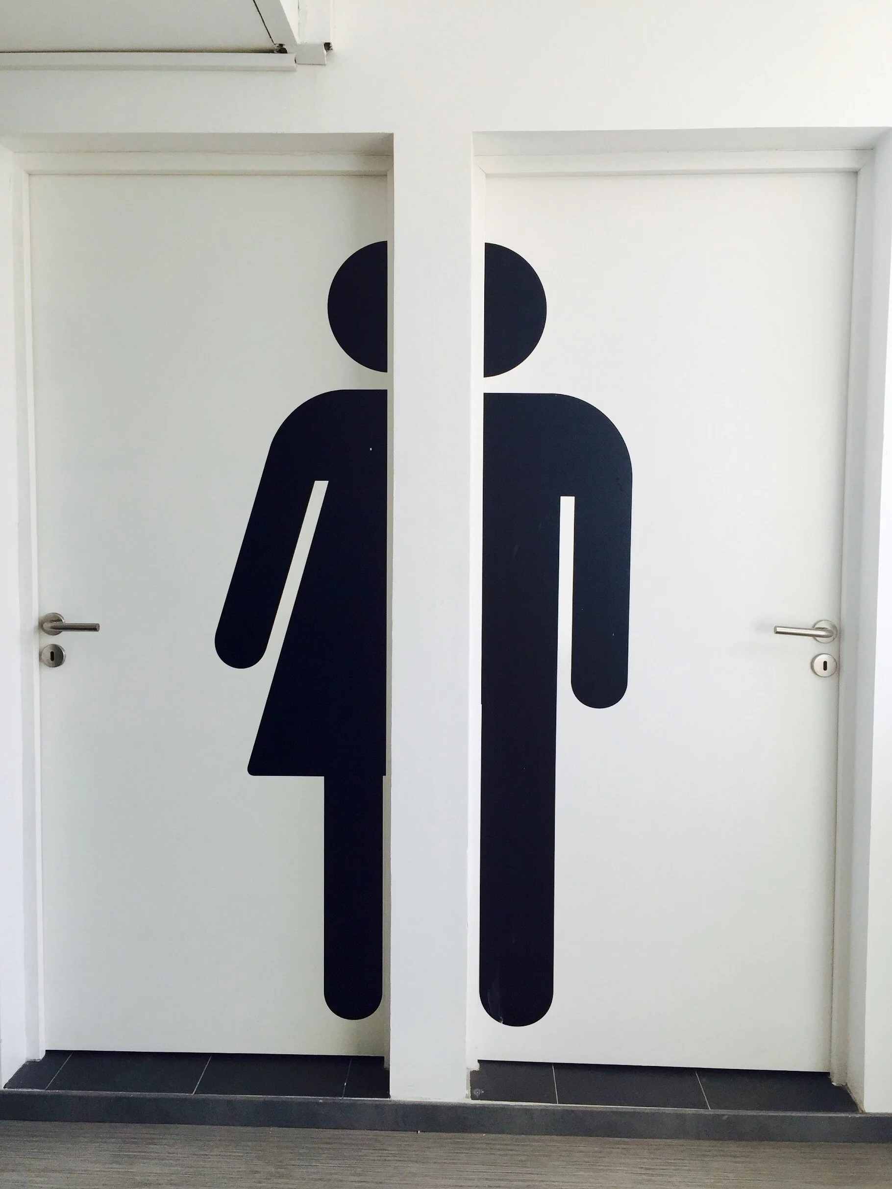 Porta de banheiro com símbolo de mulher do lado esquerdo e símbolo de homem do lado direito.