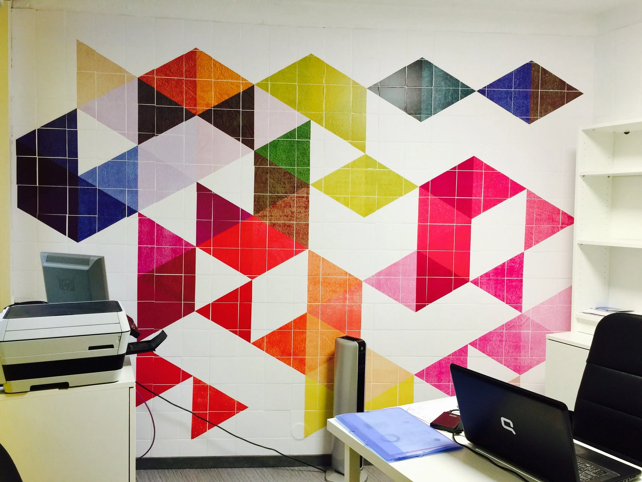 Parede decorada com mosaico de formas geométricas coloridas em um escritório.