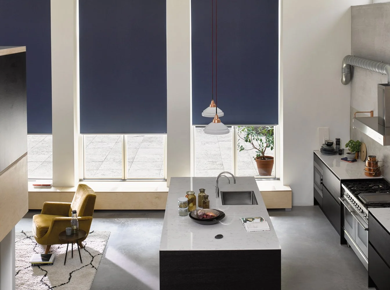 Cozinha moderna com janelas grandes, cortinas azuis, ilha central com pia, decoração minimalista, cadeira amarela de apoio, plantas e utensílios de cozinha.