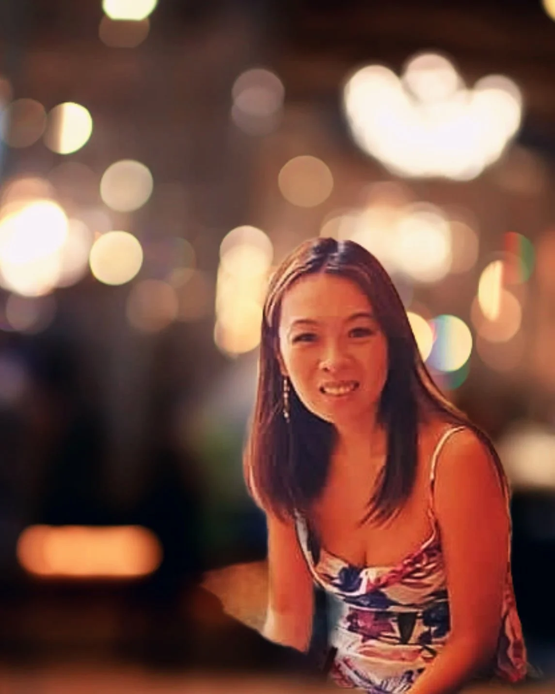 Mulher sorrindo em ambiente com luzes desfocadas ao fundo.