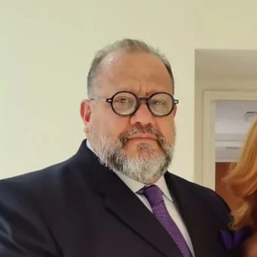 Retrato de un hombre con barba, gafas y traje oscuro, en un entorno interior