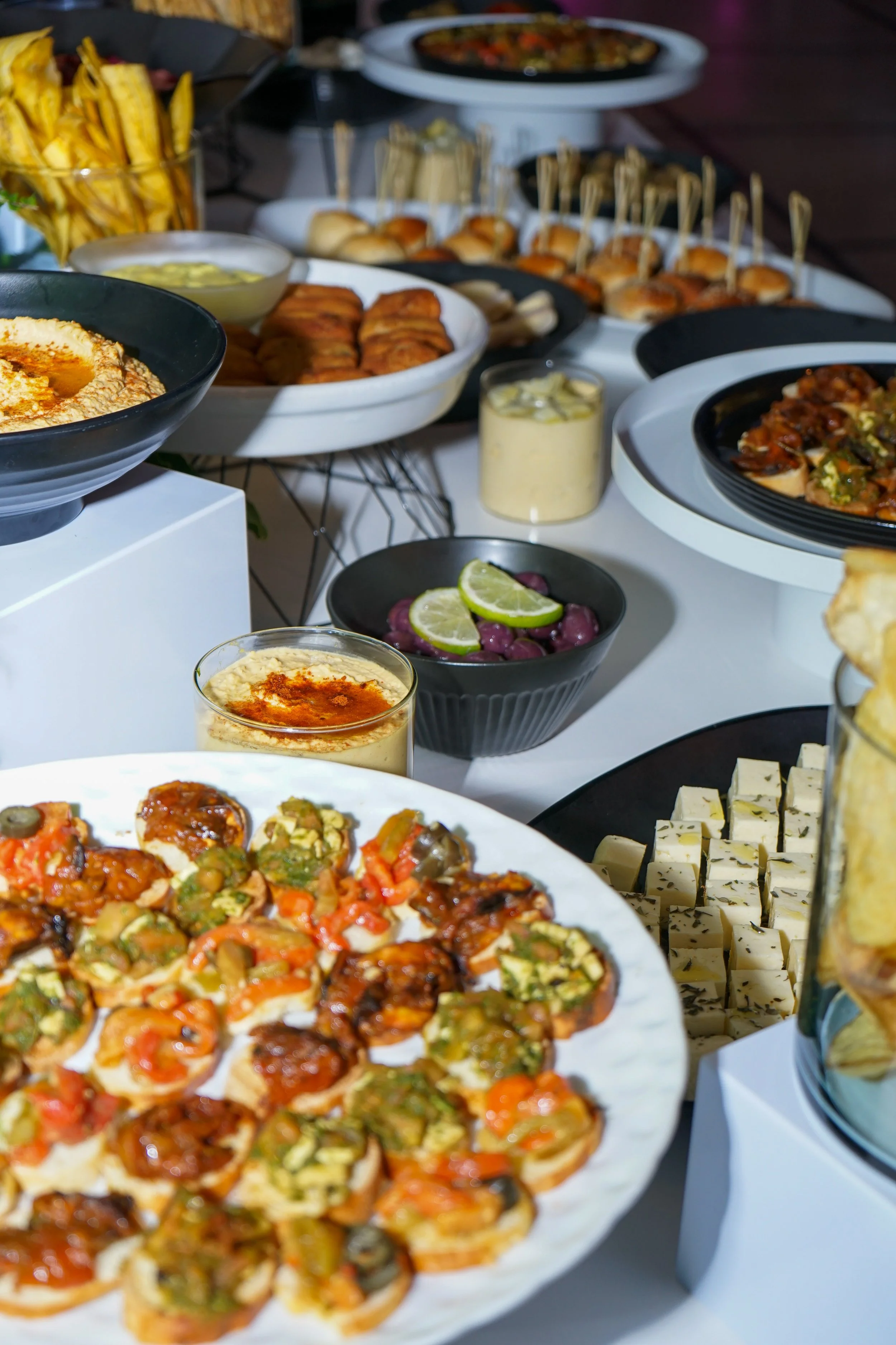 Variedad de aperitivos y tapas en un banquete, incluyendo mini pizzas, papas fritas, dip de hummus, en un ambiente festivo.