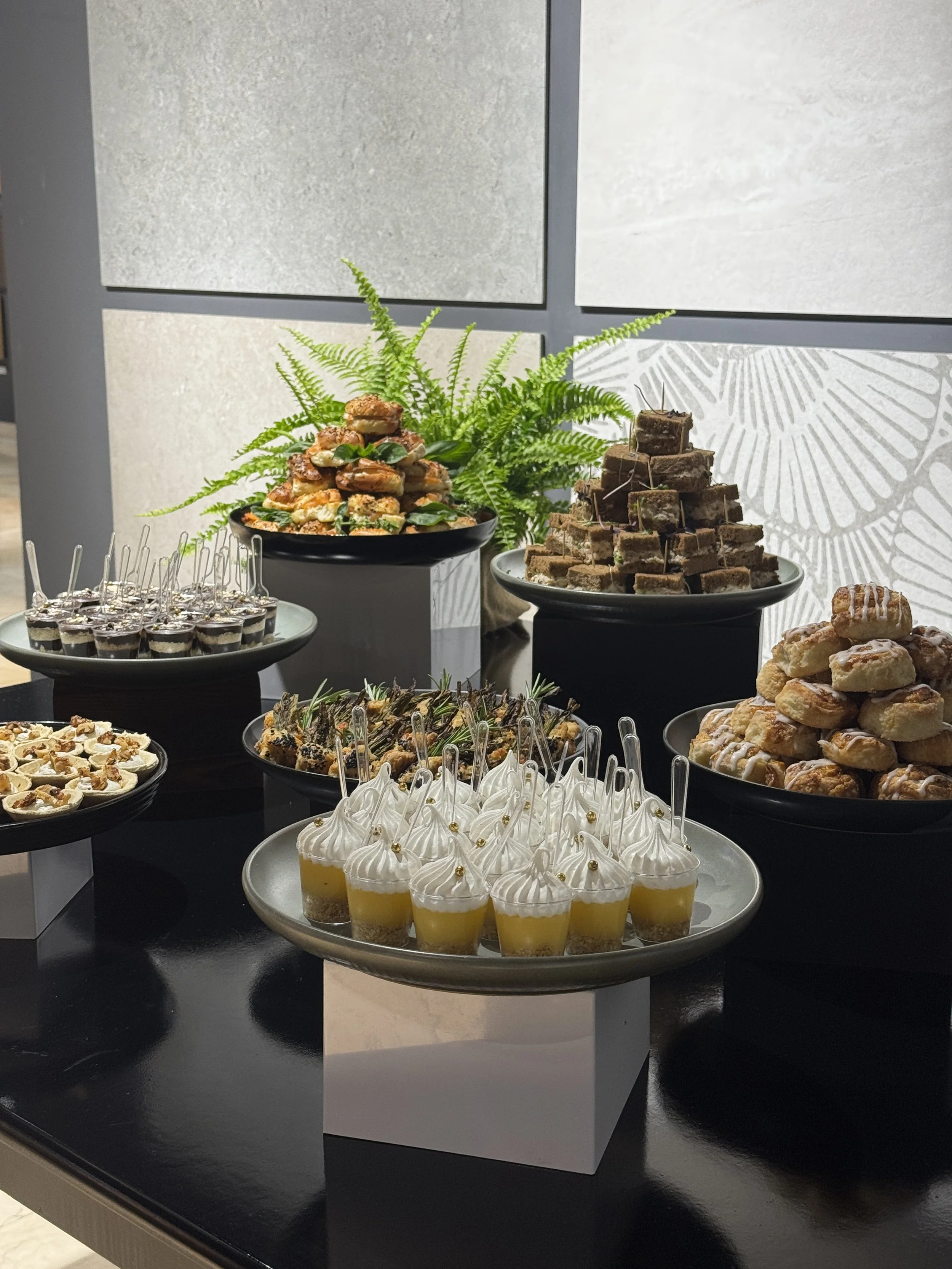Mesa con postres variados, incluyendo tartas de chocolate, vasos con gelatinas de frutas y pequeños pasteles, decorados con crema y dorados, en un evento o fiesta.