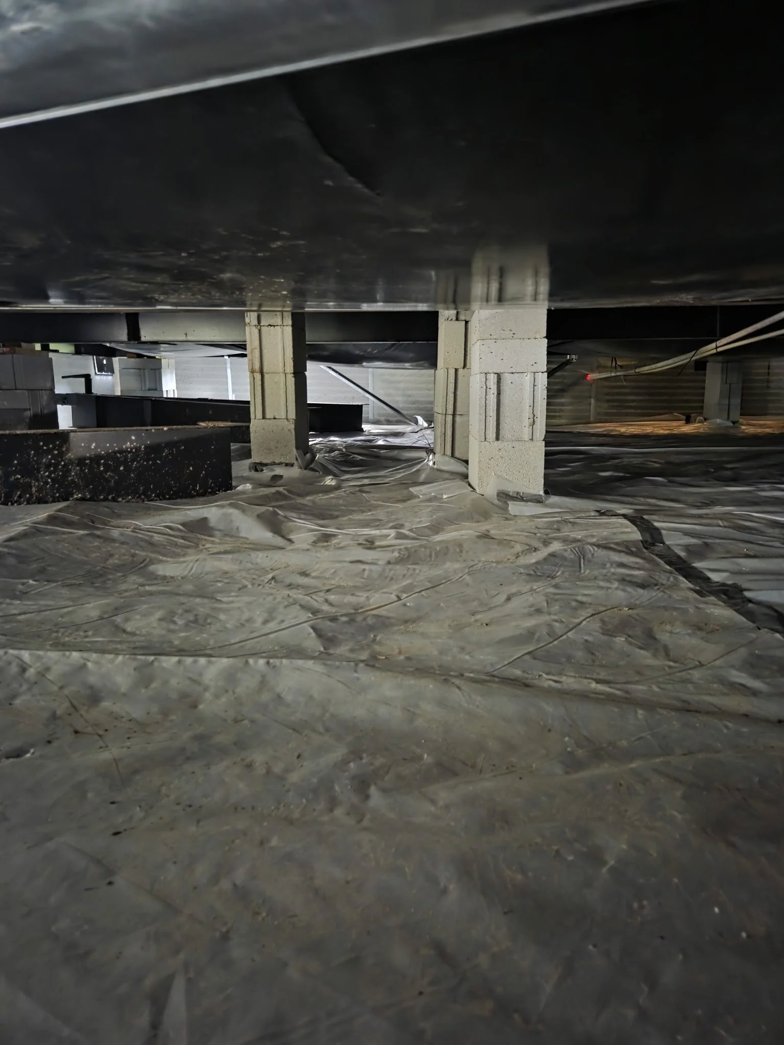 Underground parking garage with concrete pillars and a black substance on the ceiling, covered with a plastic sheet on the floor.