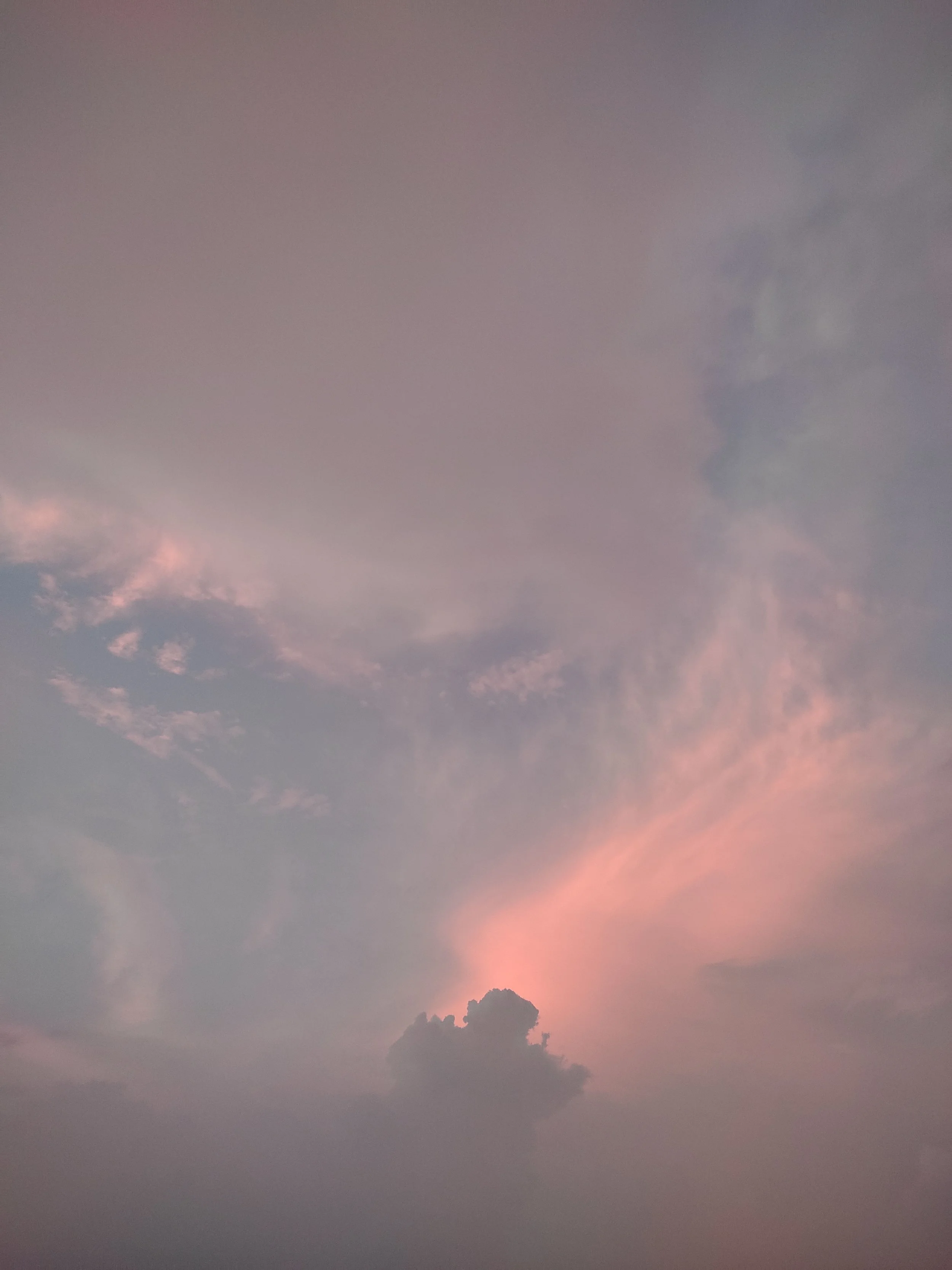 A sky at sunset with soft pink and purple clouds, and a silhouette of a mountain at the horizon.