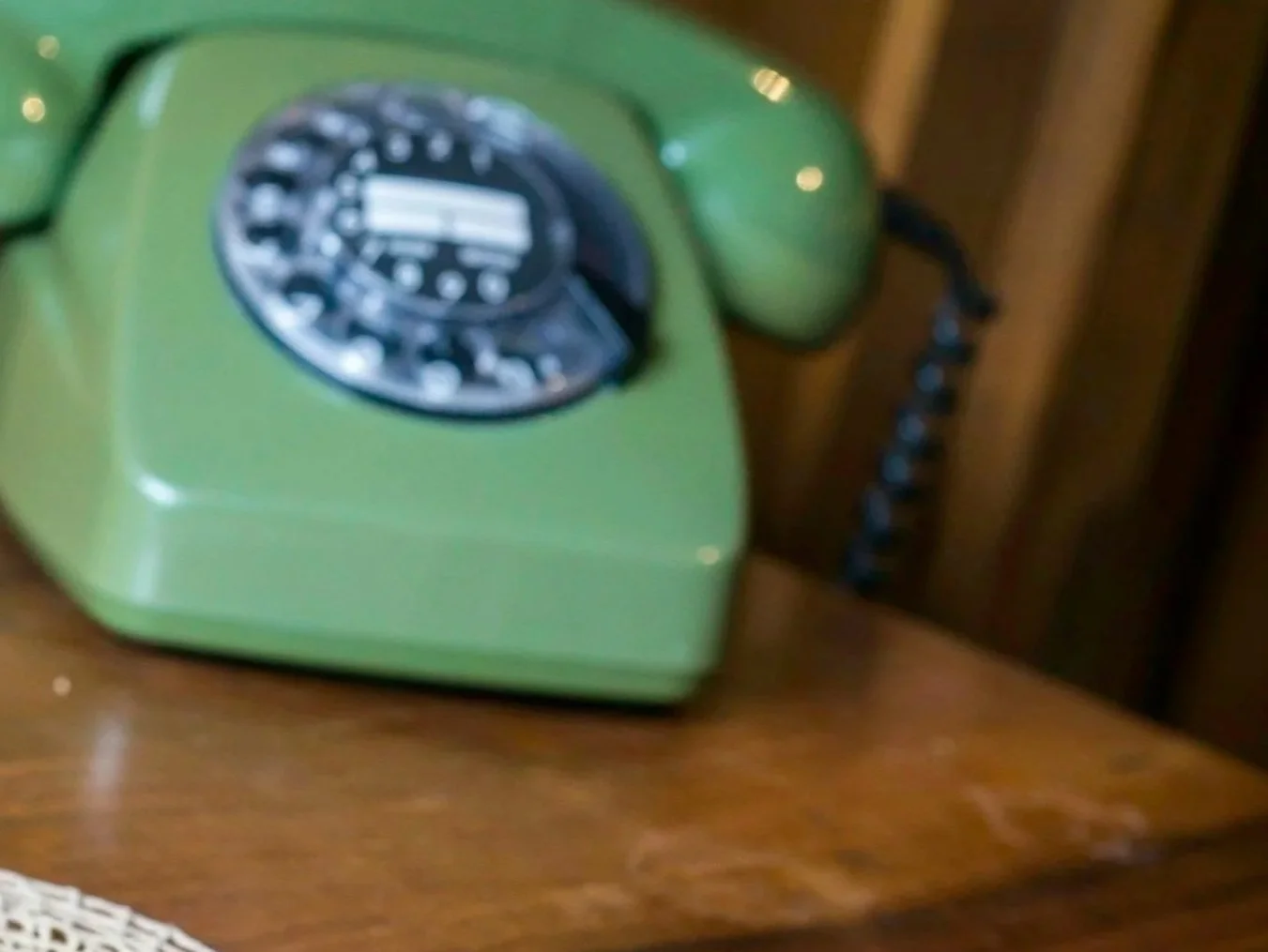 Green vintage rotary telephone on a wooden surface.
