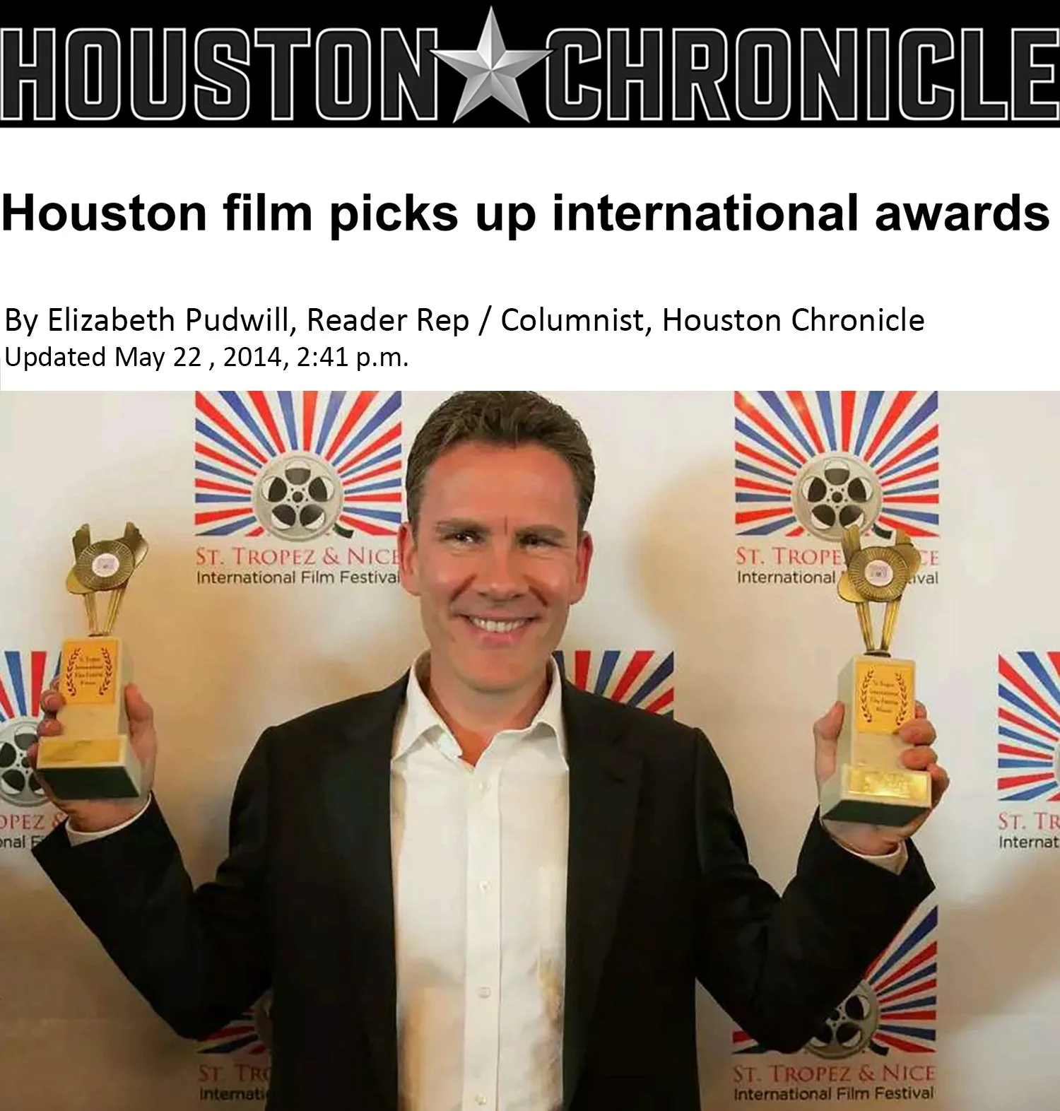 A man in a black suit holding up two gold awards at the St. Tropez & Nice International Film Festival, smiling in front of a backdrop with film reels and the festival's logo.