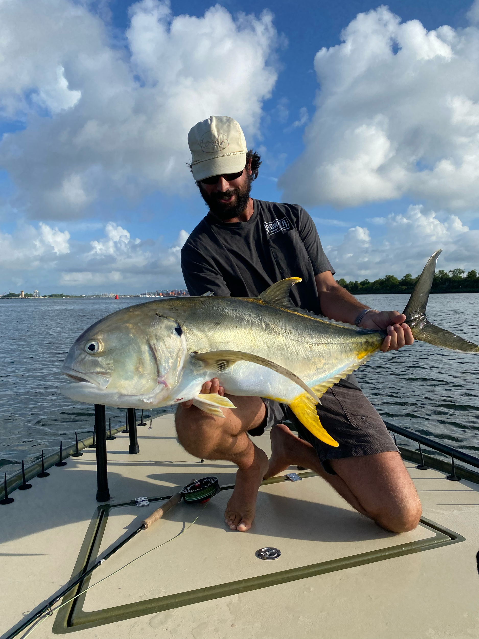 Man sitting on boat holding a large fish, with a lake and partly cloudy sky in the background.