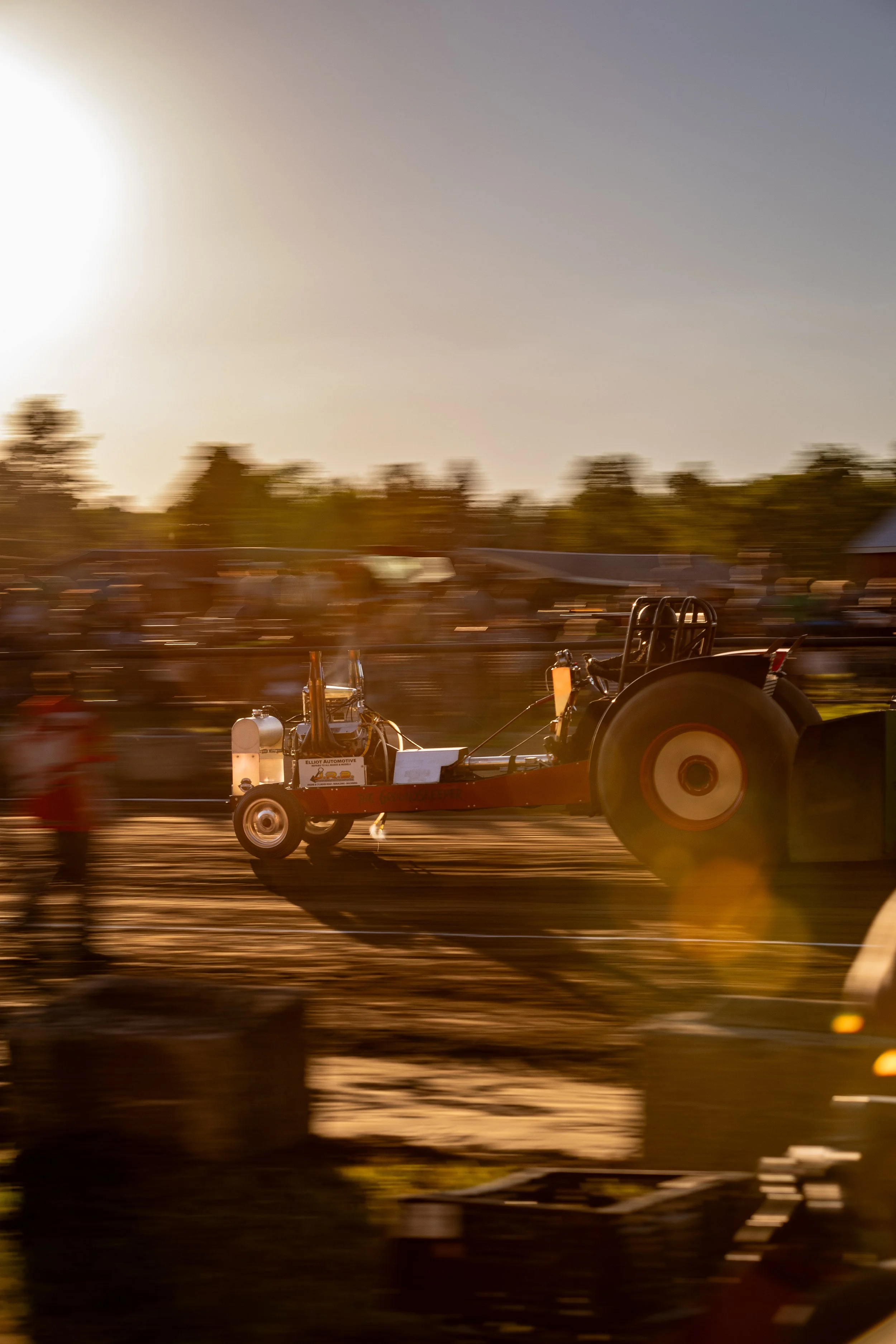 A blurred image of a tractor on a farm during sunset, with trees and a building in the background.